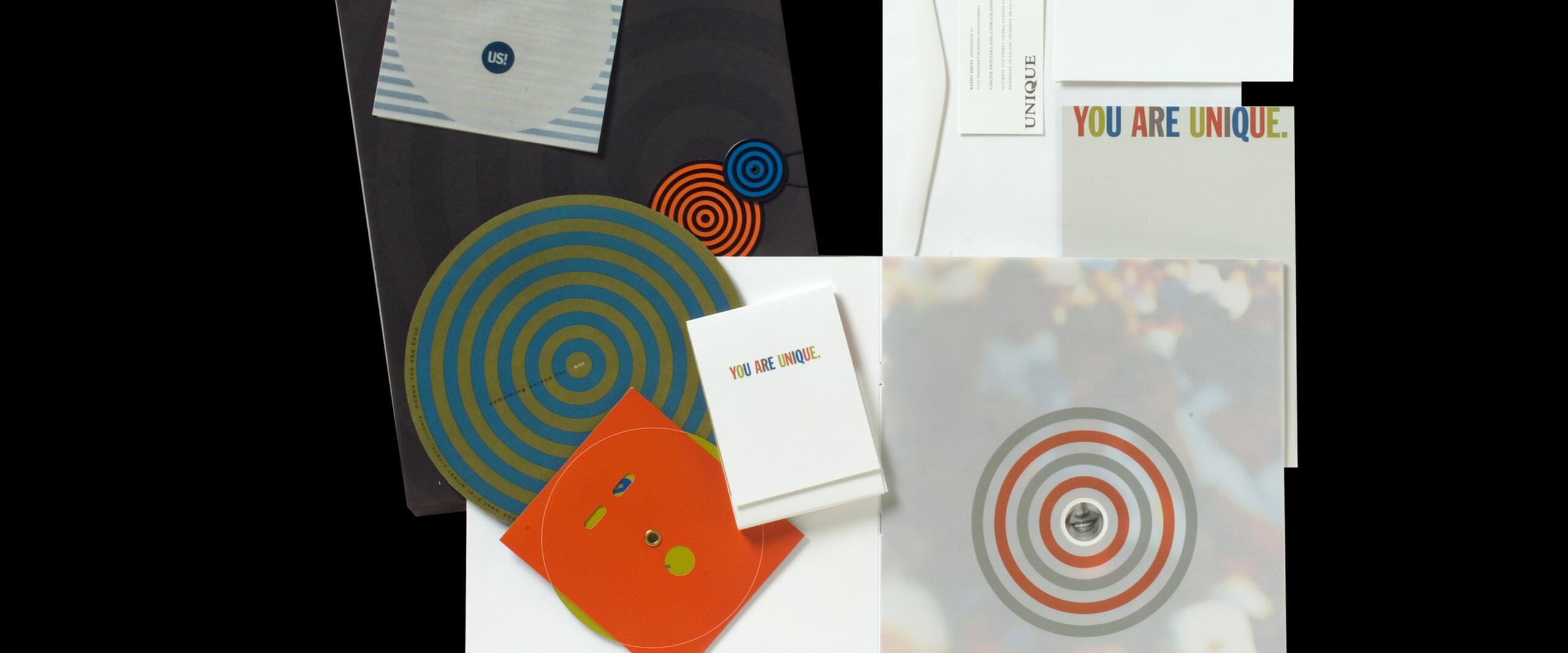 Stationery set with colorful circular patterns, envelopes, and cards featuring a message in multicolored text. The design has a modern, playful aesthetic with emphasis on uniqueness.