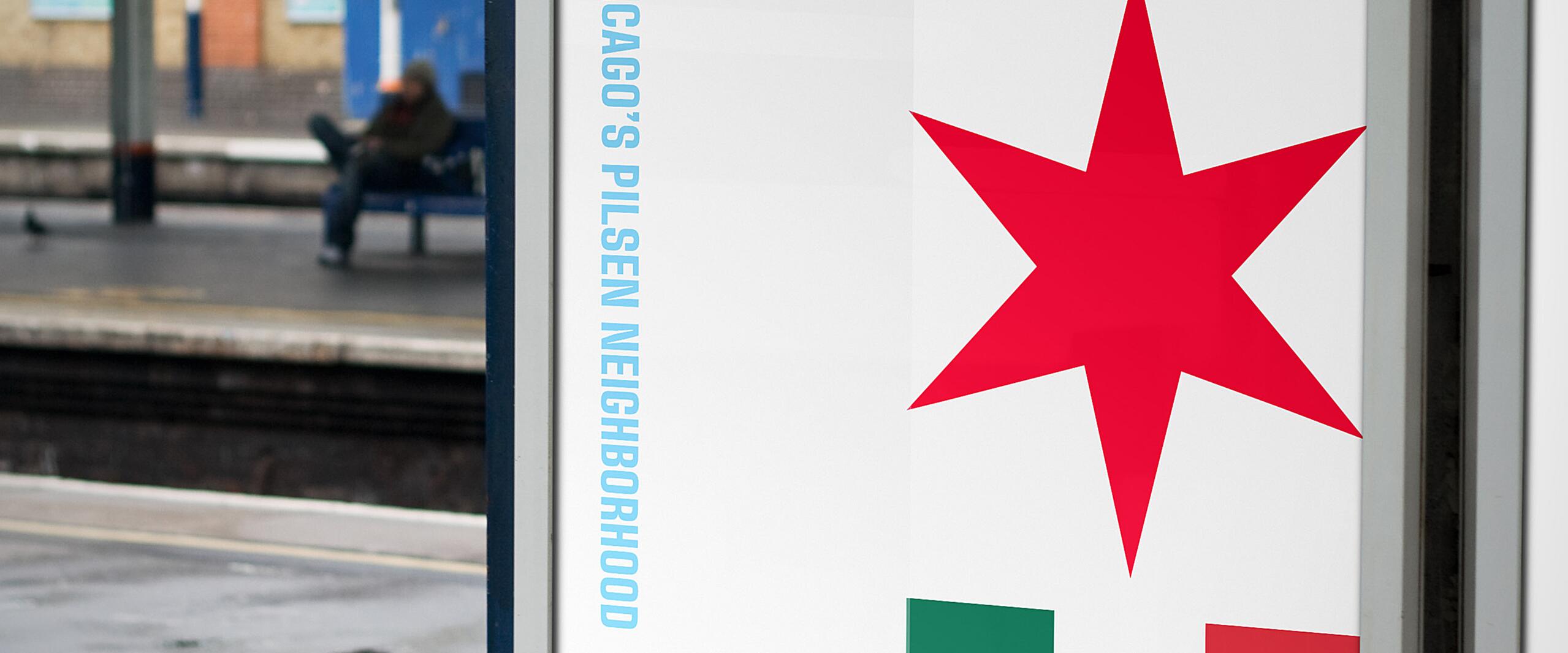 Sign at a train station platform featuring the Chicago flag star above a Mexican flag, with text welcoming to Chicago's Pilsen neighborhood. A person sits on a bench in the background.