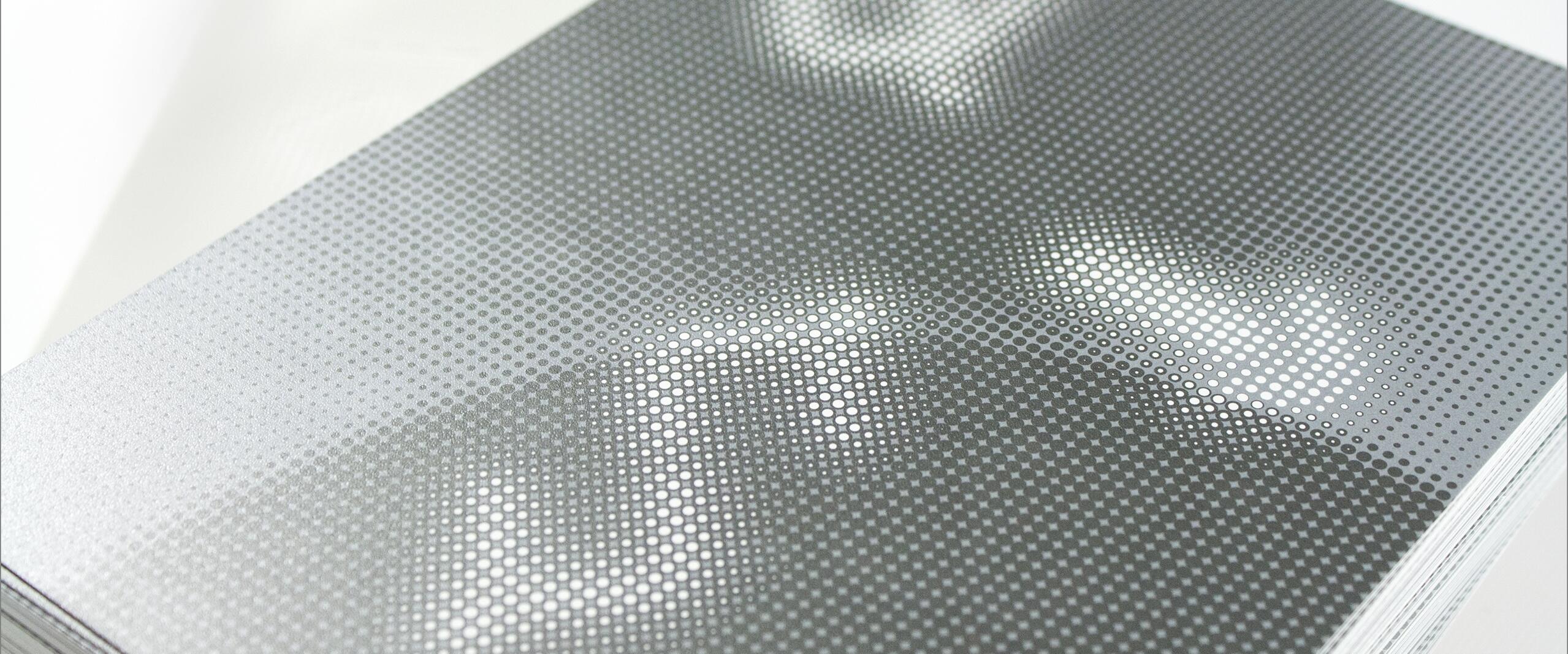 Close-up of a stack of glossy brochures with a pixelated pattern and abstract design in white and gray, featuring prominent dot textures.