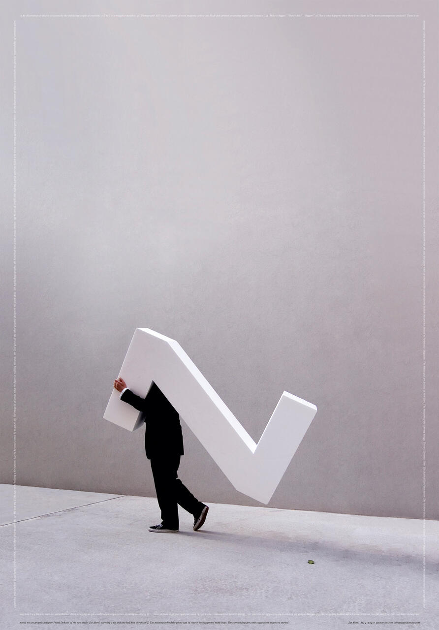 A person in a suit walks while holding a large white checkmark-shaped object against a plain background.