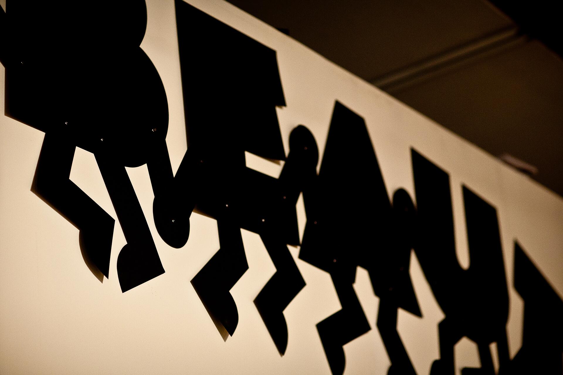 Black silhouetted figures with geometric shapes on a white background, casting shadows.
