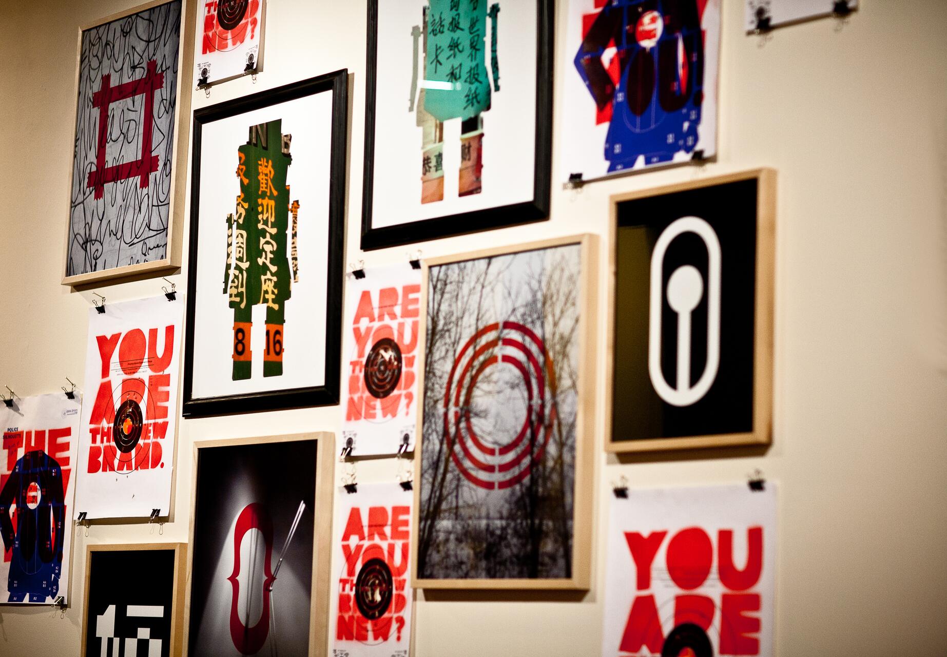 A wall adorned with various framed artworks and posters featuring abstract designs, typography, and patterns in vibrant colors like red, black, and green.