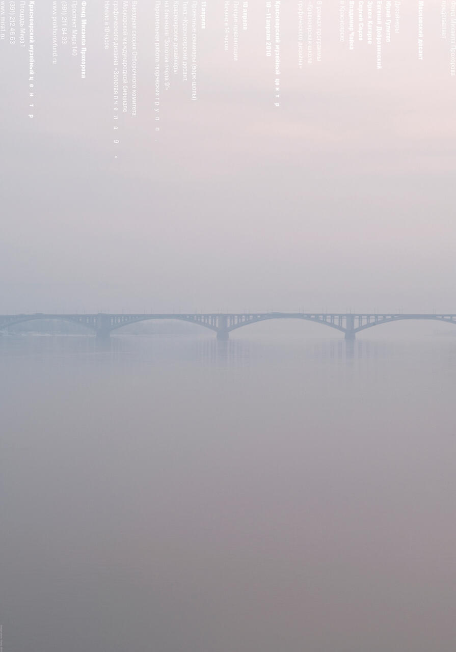 A long bridge stretches over a calm, misty body of water under a hazy, pale sky.