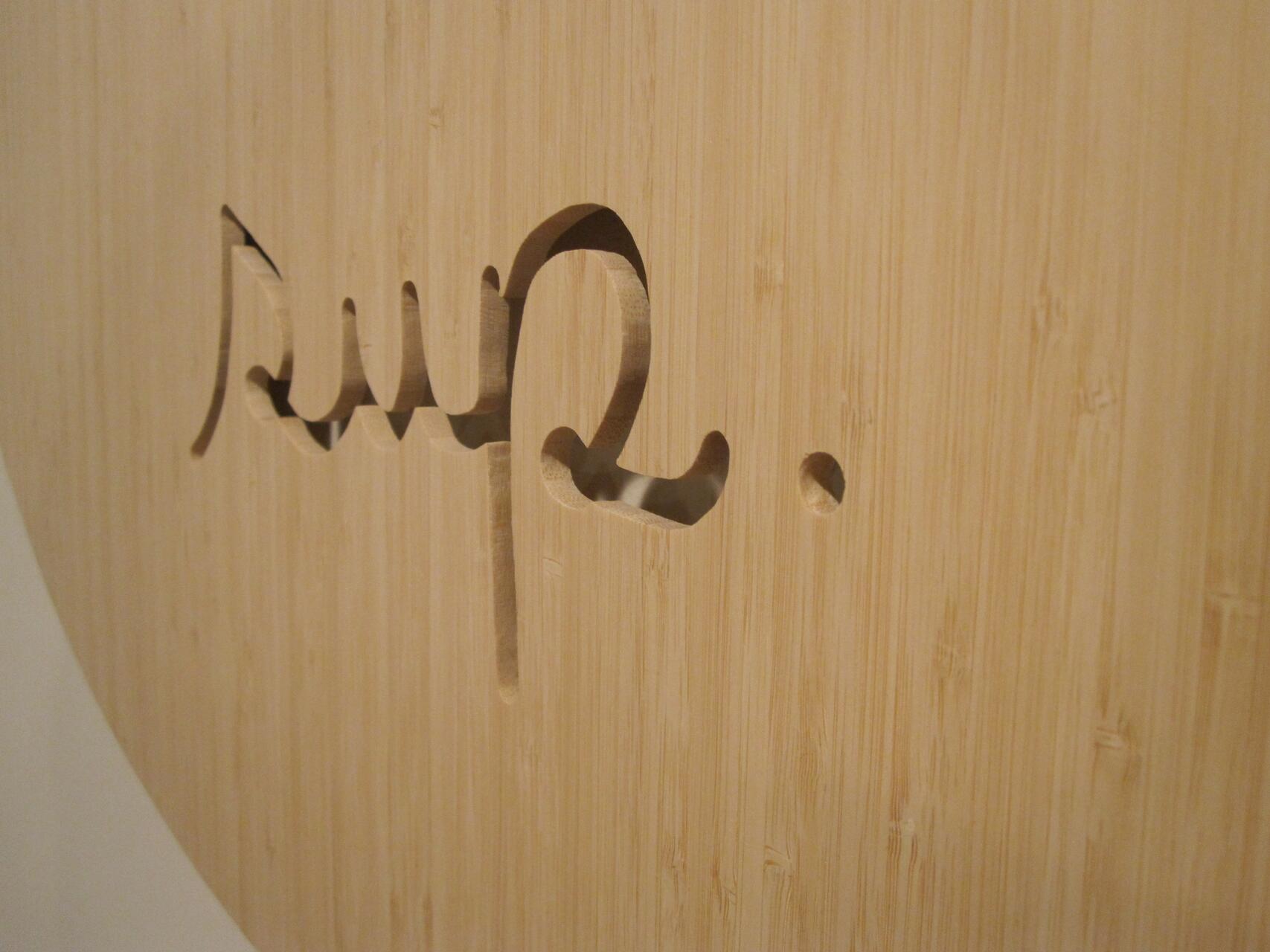 Bamboo surface with text cut out, showing a calligraphic design and a small circle.