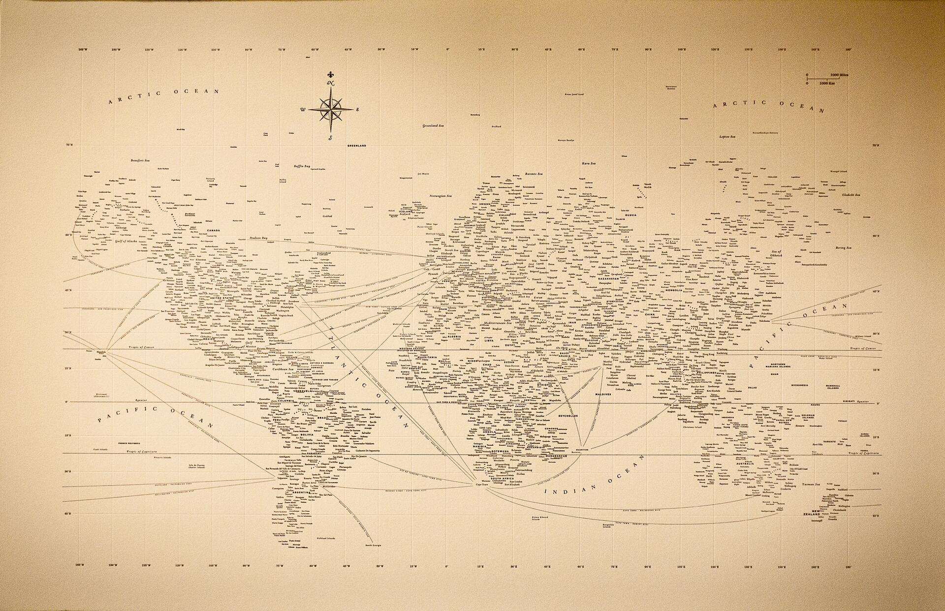 Sepia-toned world map with various names and routes marked across continents and oceans, featuring a compass rose for navigation.
