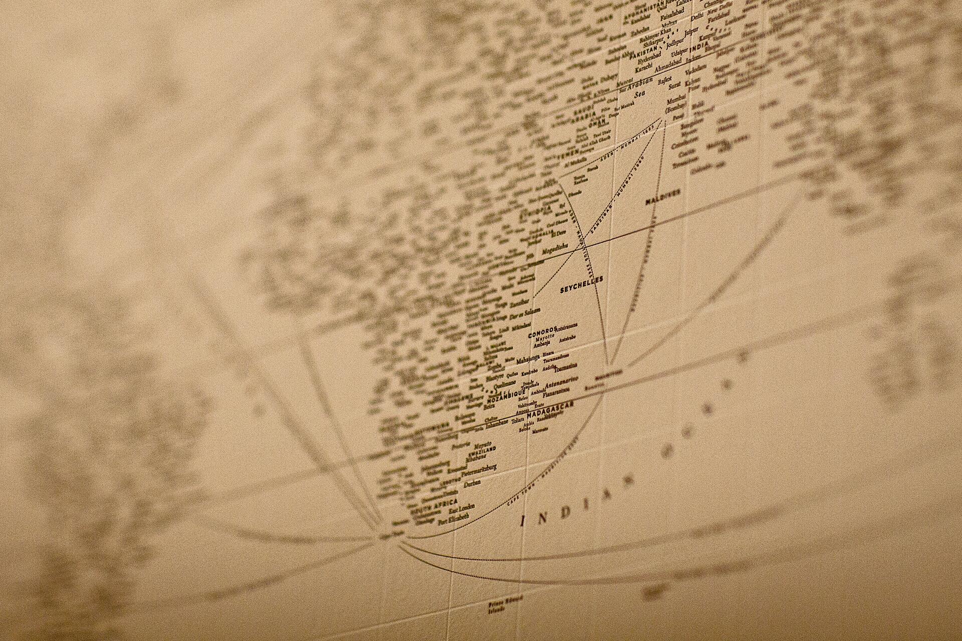 Sepia-toned close-up of a world map focusing on the Indian Ocean, showing country names like Madagascar and Seychelles, with surrounding network lines.