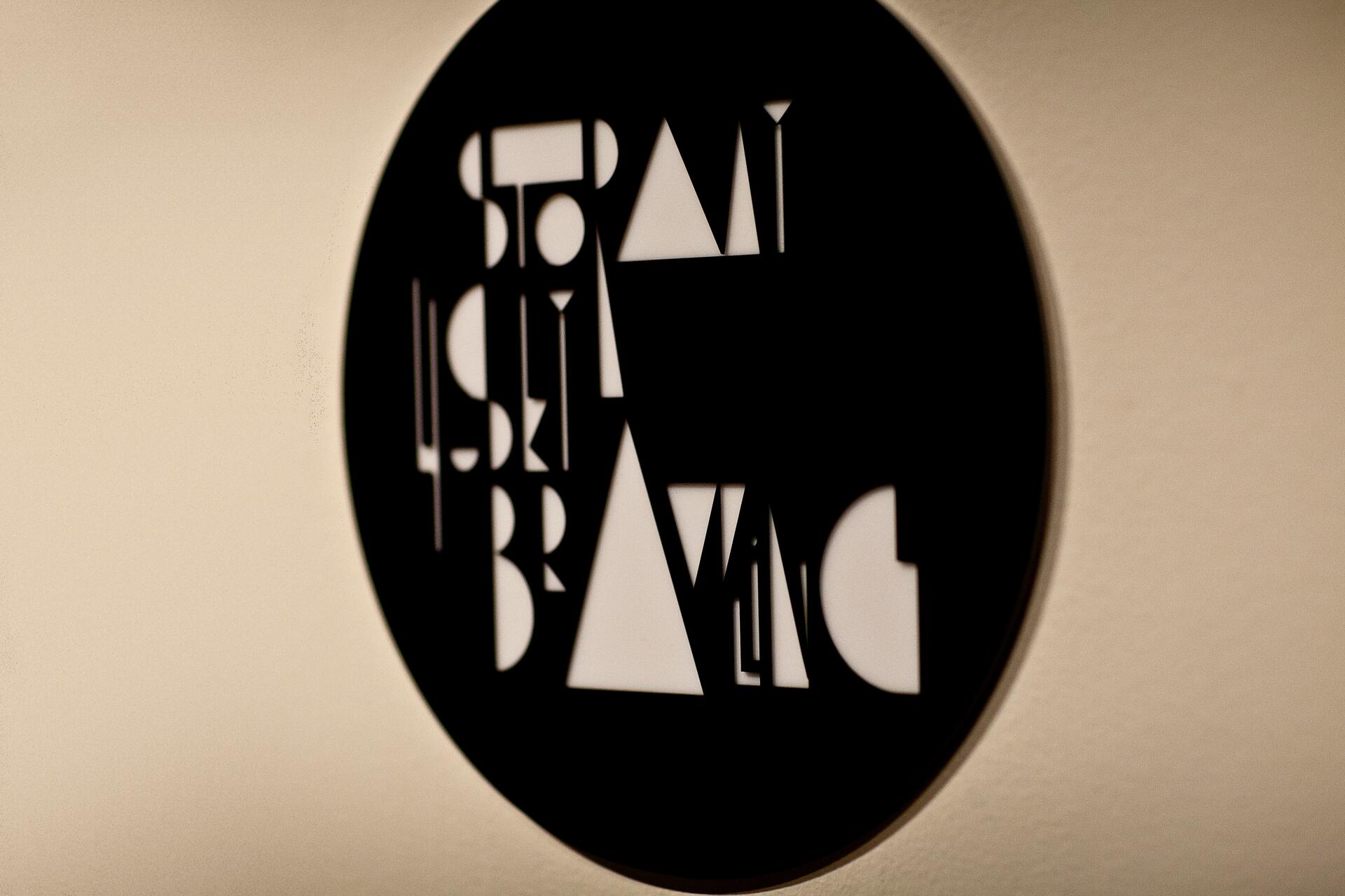 Black circular wall art with abstract cutout letters, casting a shadow on a beige wall.