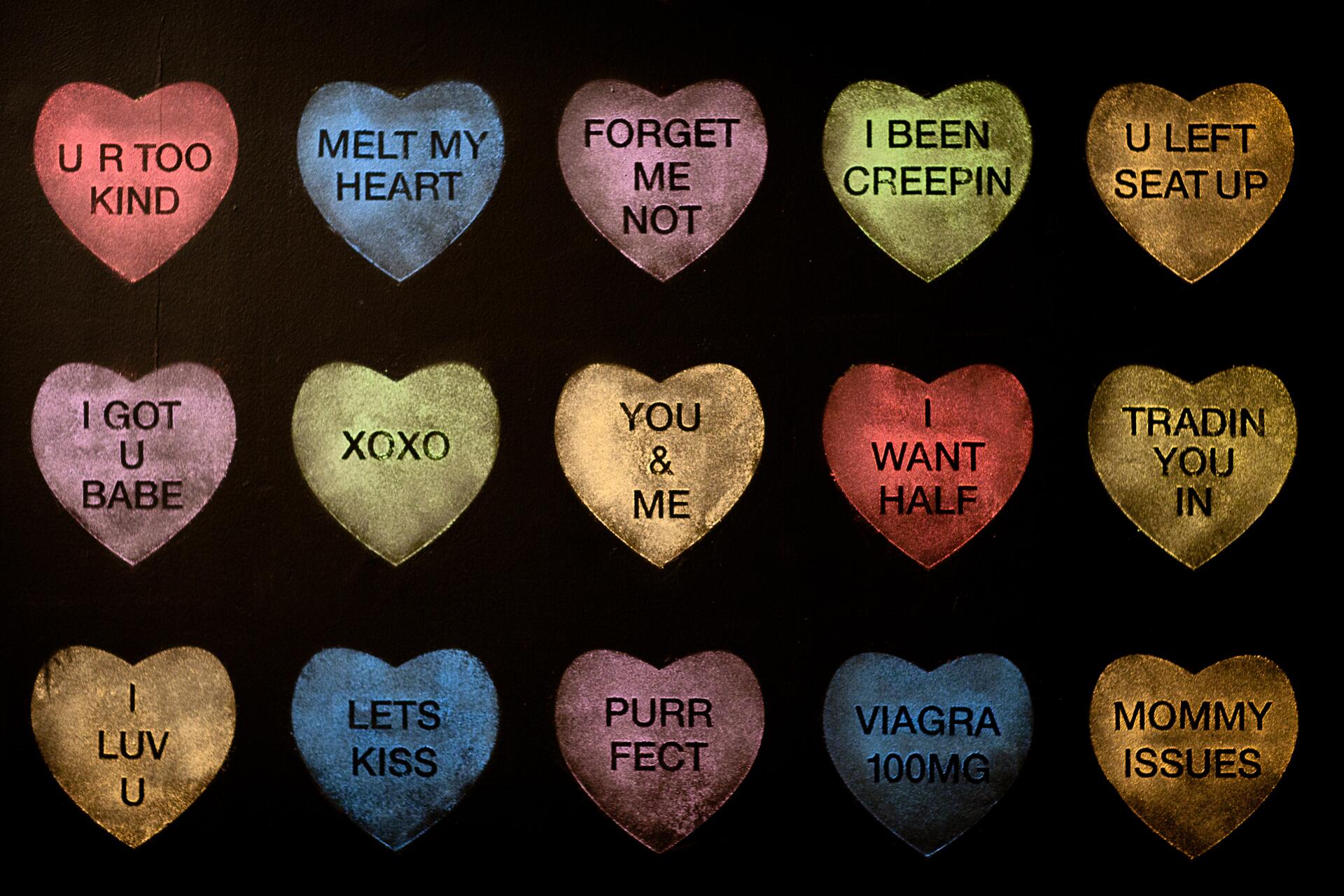Colorful candy hearts with playful and humorous phrases, set against a black background.