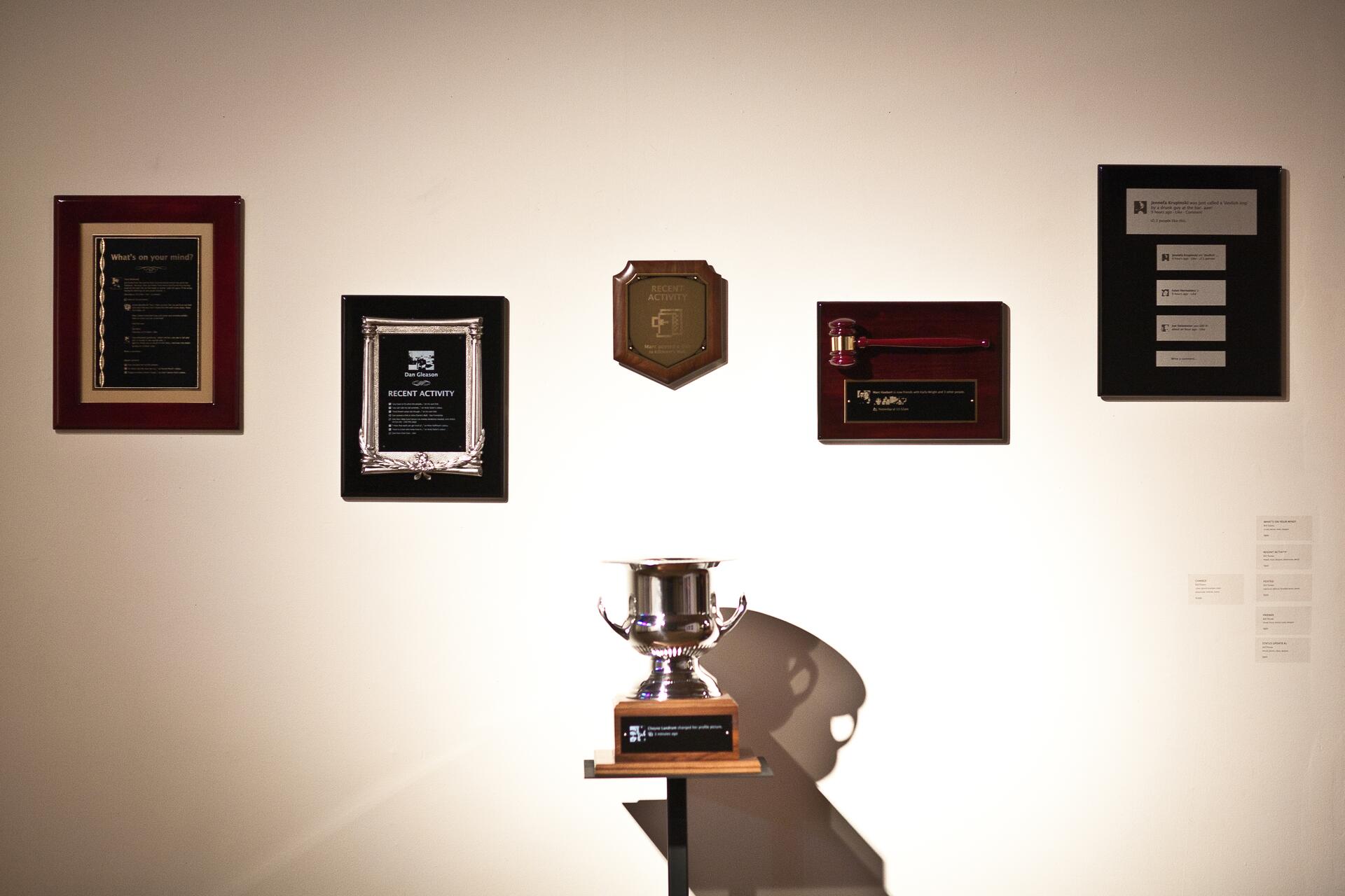 Awards and plaques on a wall, with a silver trophy centered below on a stand.