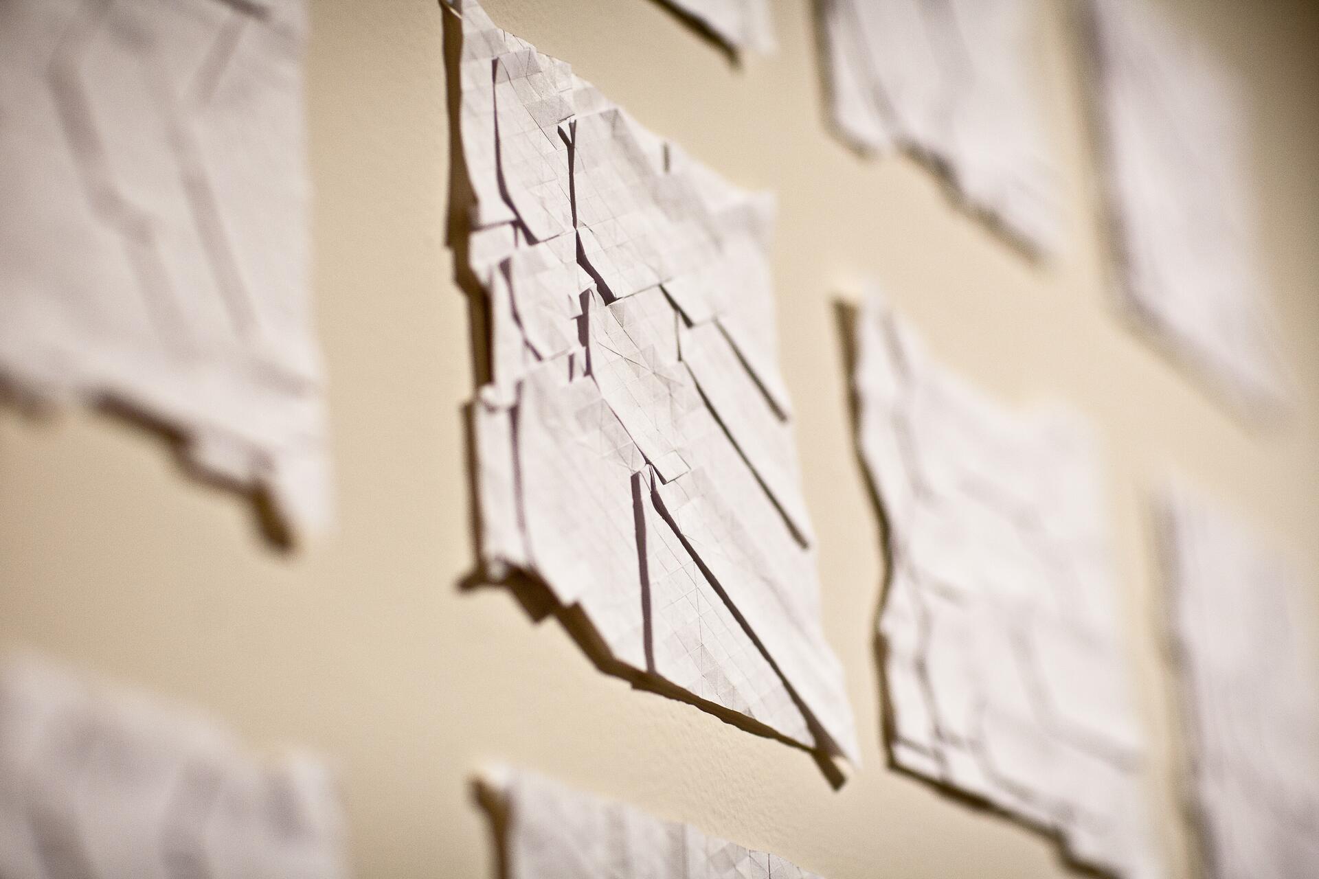 Multiple origami paper pieces with geometric folds mounted on a wall in soft lighting.