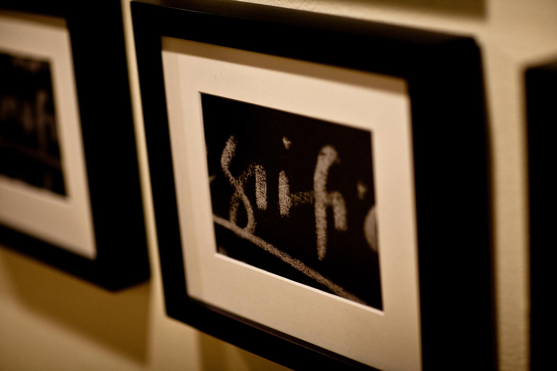 Framed photograph with partially visible chalk-like writing on a black background, hanging on a wall.