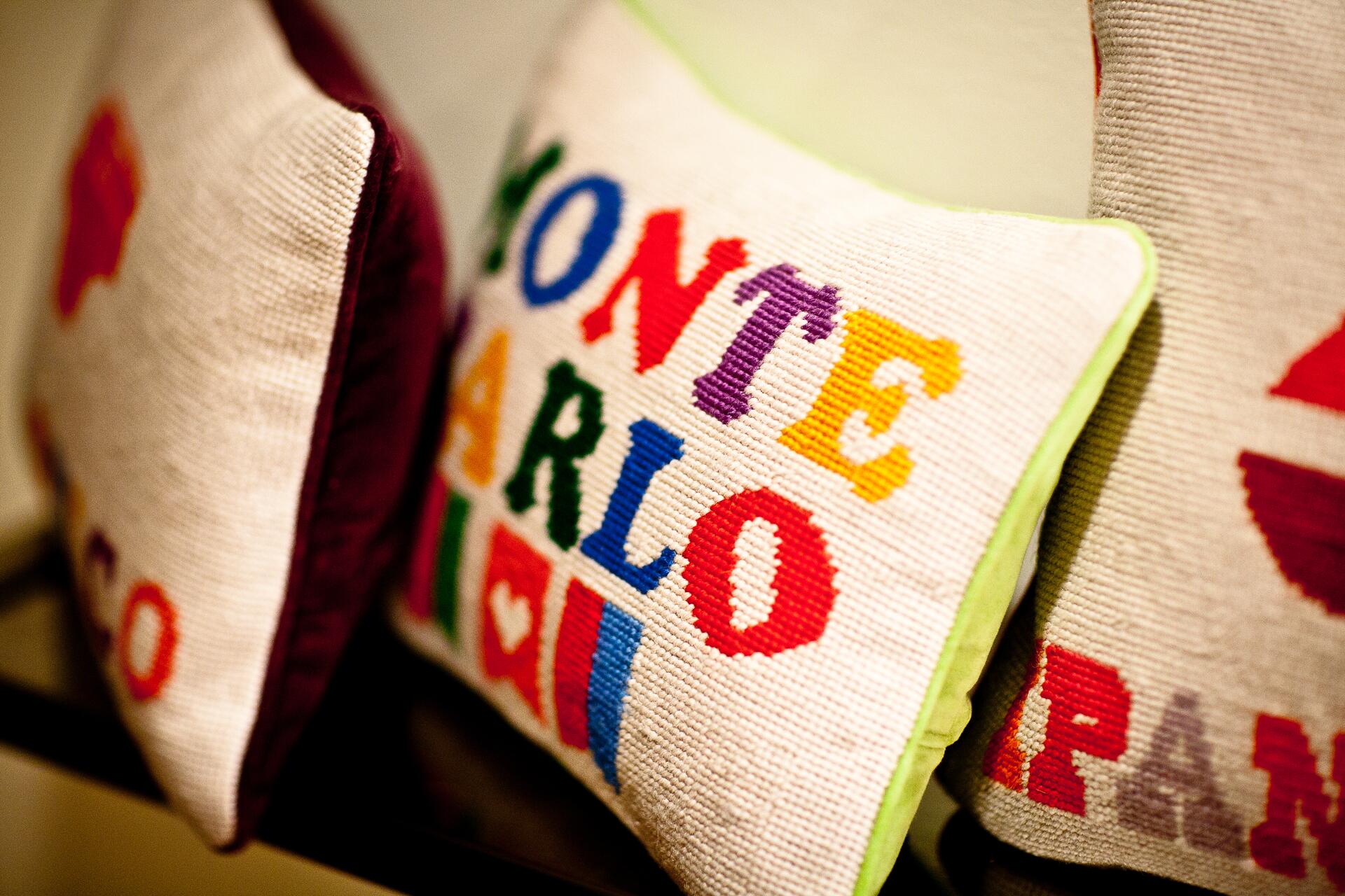 Colorful decorative pillows with embroidered letters in various hues, featuring the words "MONTE CARLO" in bold, playful font.