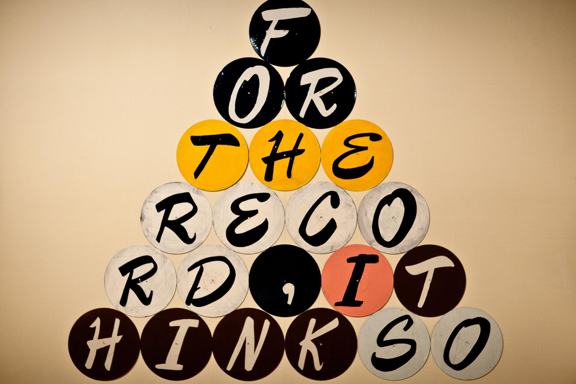 Colorful circular plaques arranged in a pyramid shape against a neutral background, with letters spelling out a phrase.