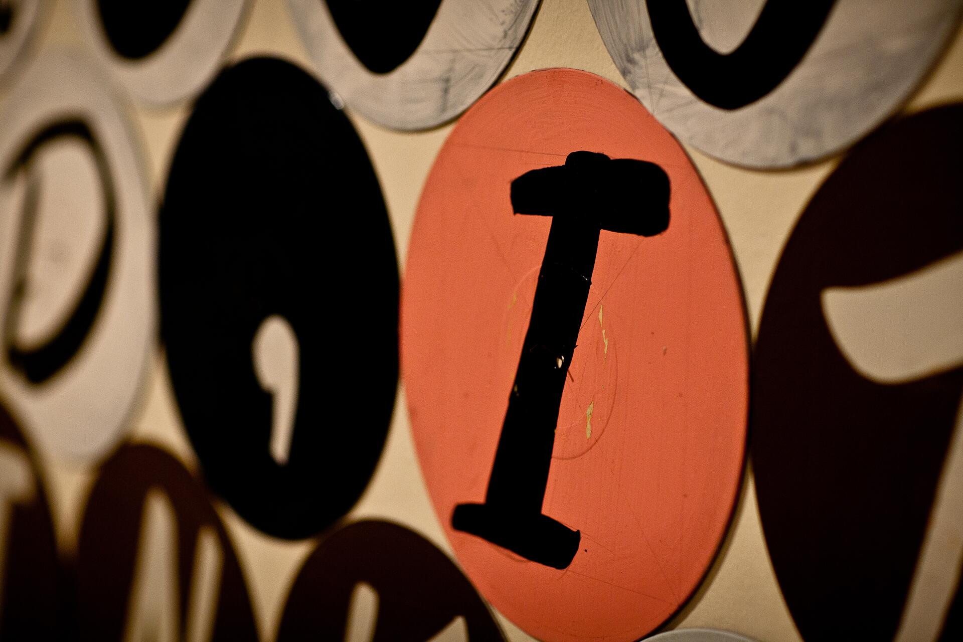 A wall collage featuring large, circular shapes with letters; a prominent uppercase black "I" on an orange background stands out amidst other letters on black and white circles.
