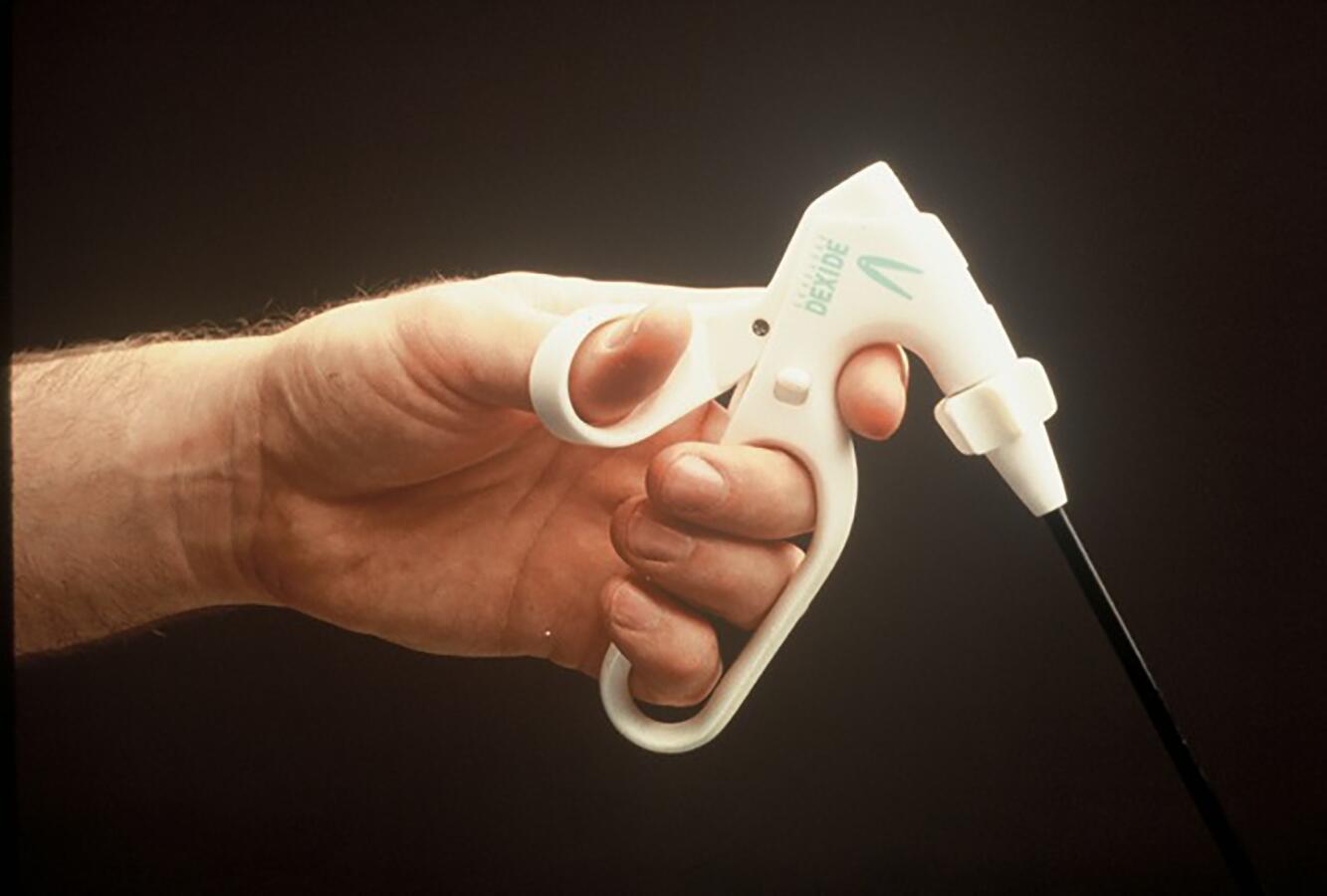 Hand holding a white plastic trigger sprayer with a black nozzle against a dark background.