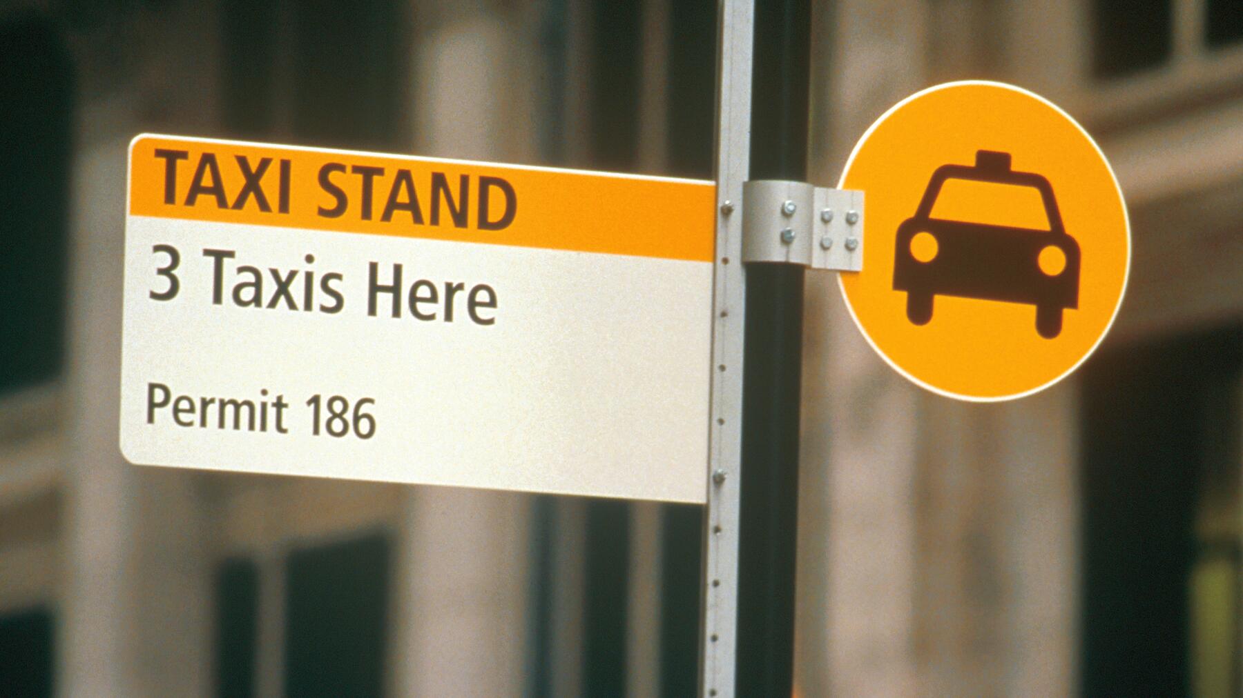 Taxi stand sign with a yellow background, permitting 3 taxis, marked Permit 186. Adjacent is a circular icon of a taxi on a pole.