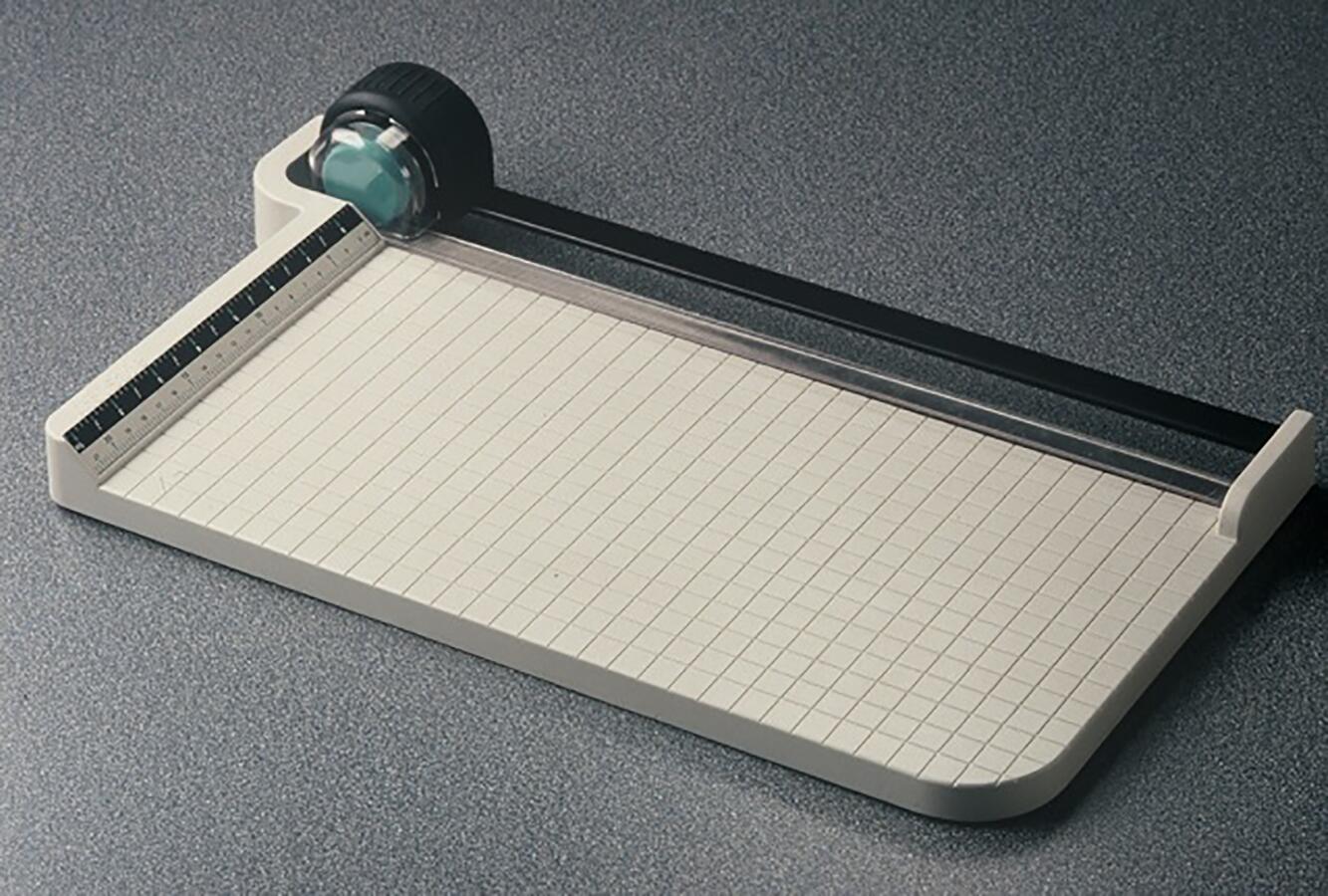 Paper cutter on a speckled gray surface, featuring a grid pattern cutting base and a black rotary blade with a measuring guide on the side.