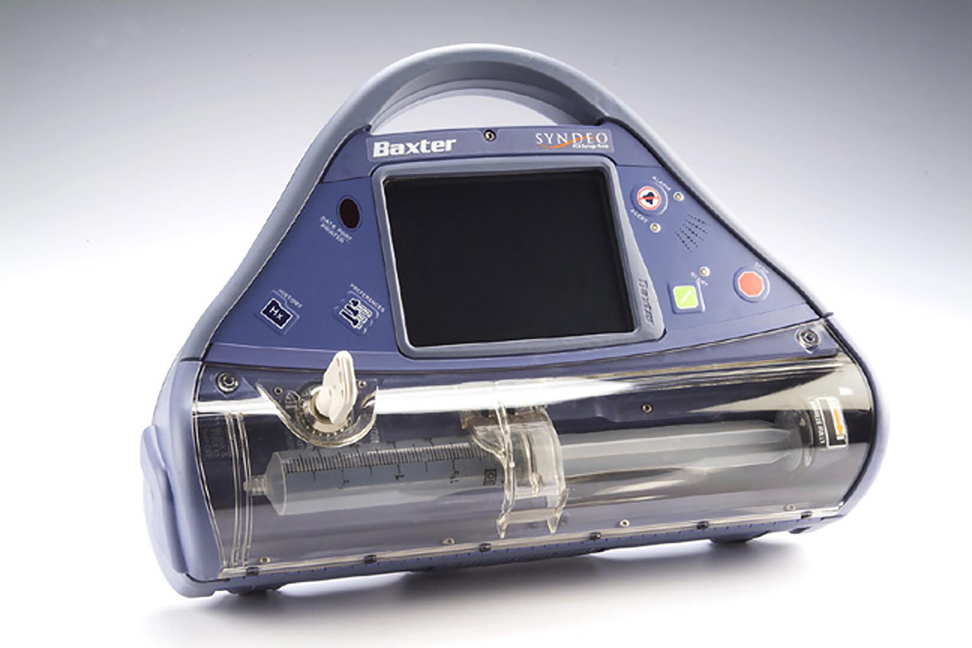 Medical device with a blue and gray casing, featuring a digital display, control buttons, and a syringe holder. The design is compact with a handle on top, used for administering precise doses of medication.