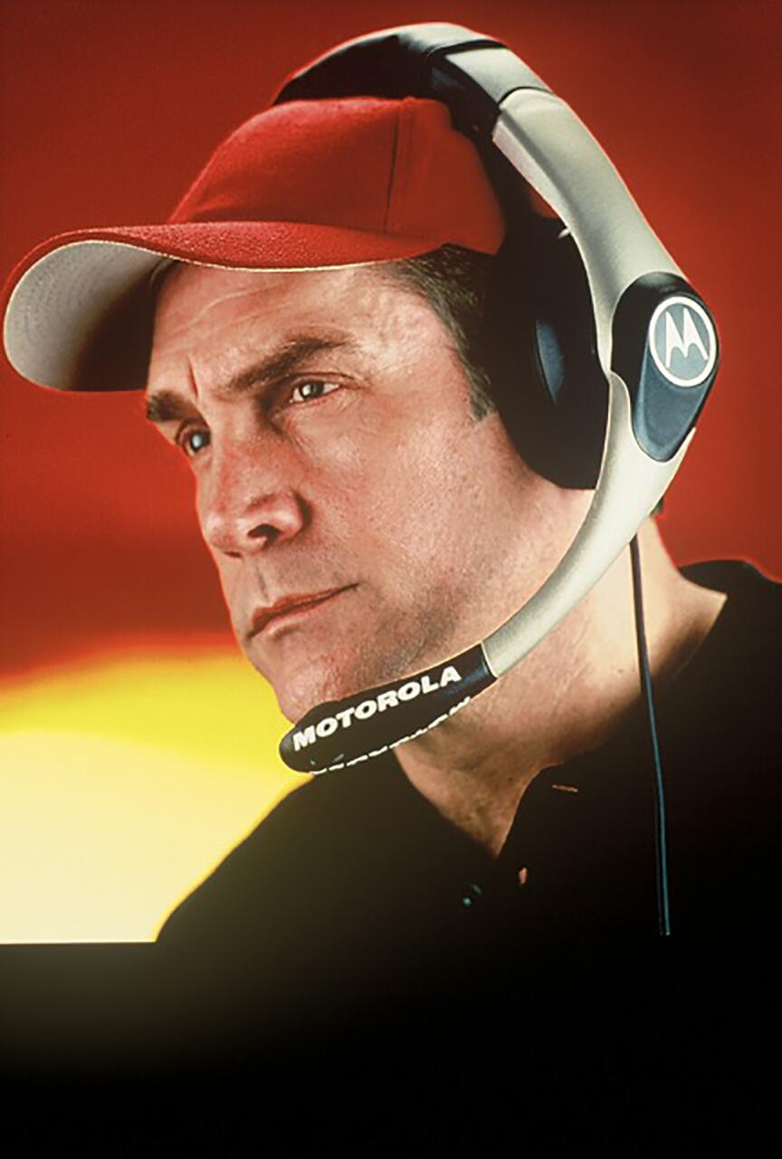 Man in a red cap wearing a Motorola headset with a microphone, against a vibrant red and yellow background.