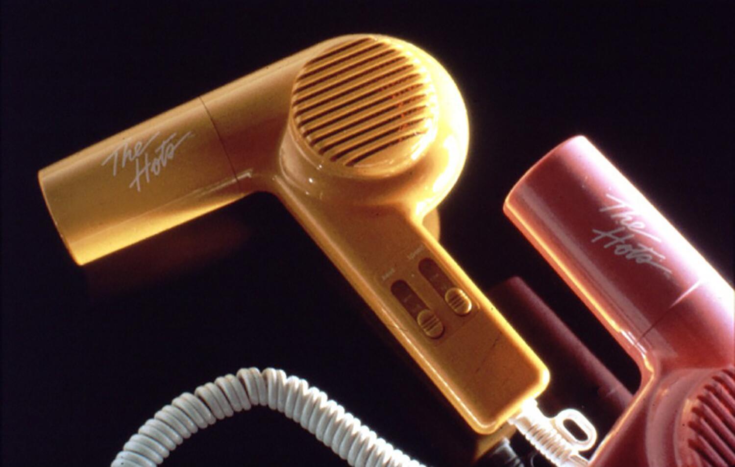 Yellow and pink hair dryers with coiled cord on black background.