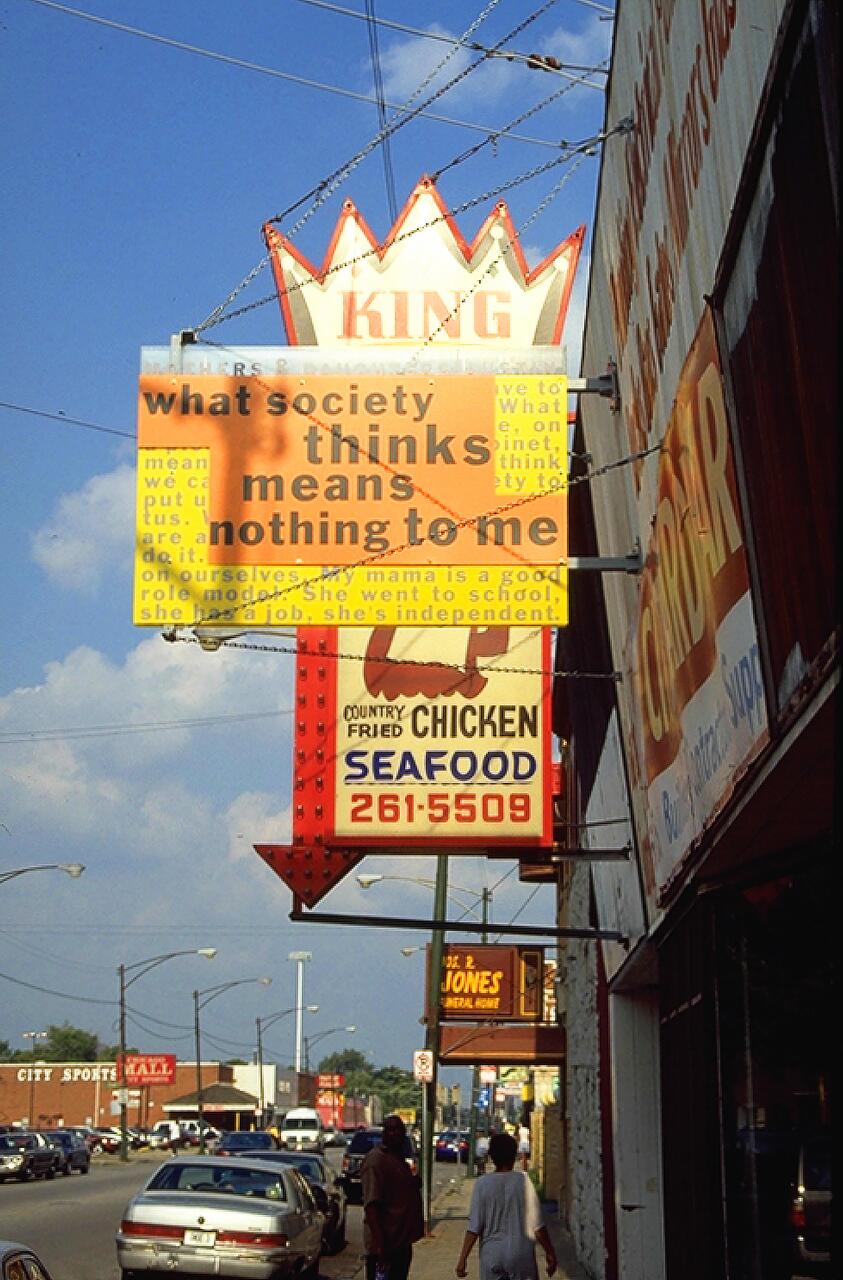 Outdoor street scene with vintage signs on a storefront, including a crown-shaped "KING" sign. Below, text in decorative fonts reads "COUNTRY FRIED CHICKEN SEAFOOD" with a phone number. Sidewalk with pedestrians, parked cars, and a cloudy sky.