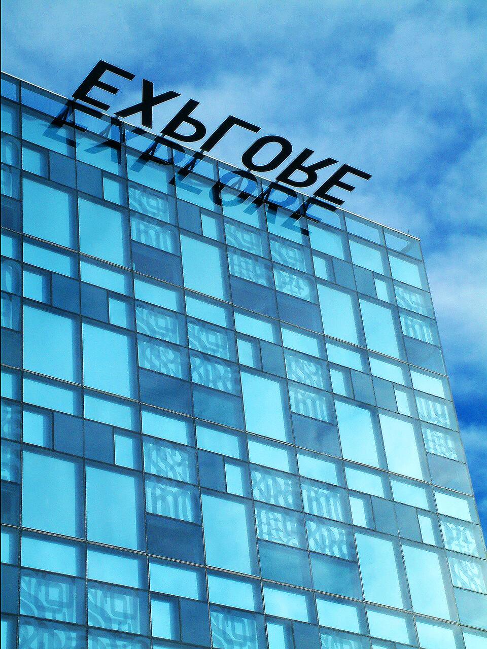 Modern glass building with reflective blue panels against a partly cloudy sky.