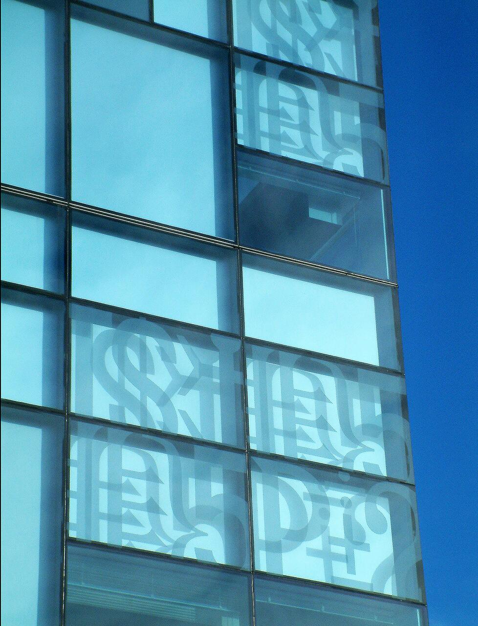Glass building facade with abstract patterns, reflecting blue sky.