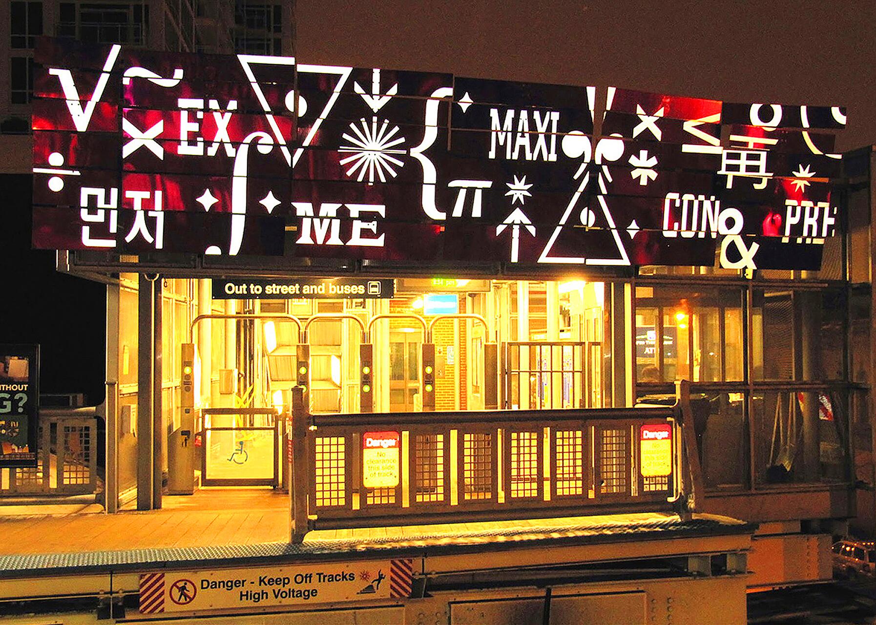 Illuminated train station entrance at night with a colorful sign featuring abstract symbols and letters.