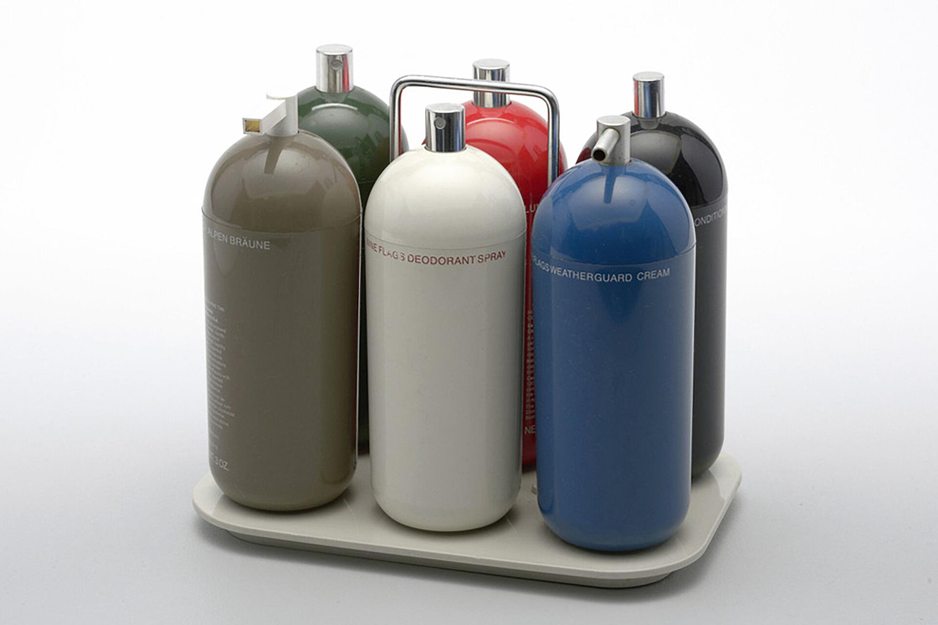Set of colorful, cylindrical bottles with metal caps organized on a tray. The bottles are green, white, gray, red, black, and blue, with a silver handle on the tray for easy carrying.
