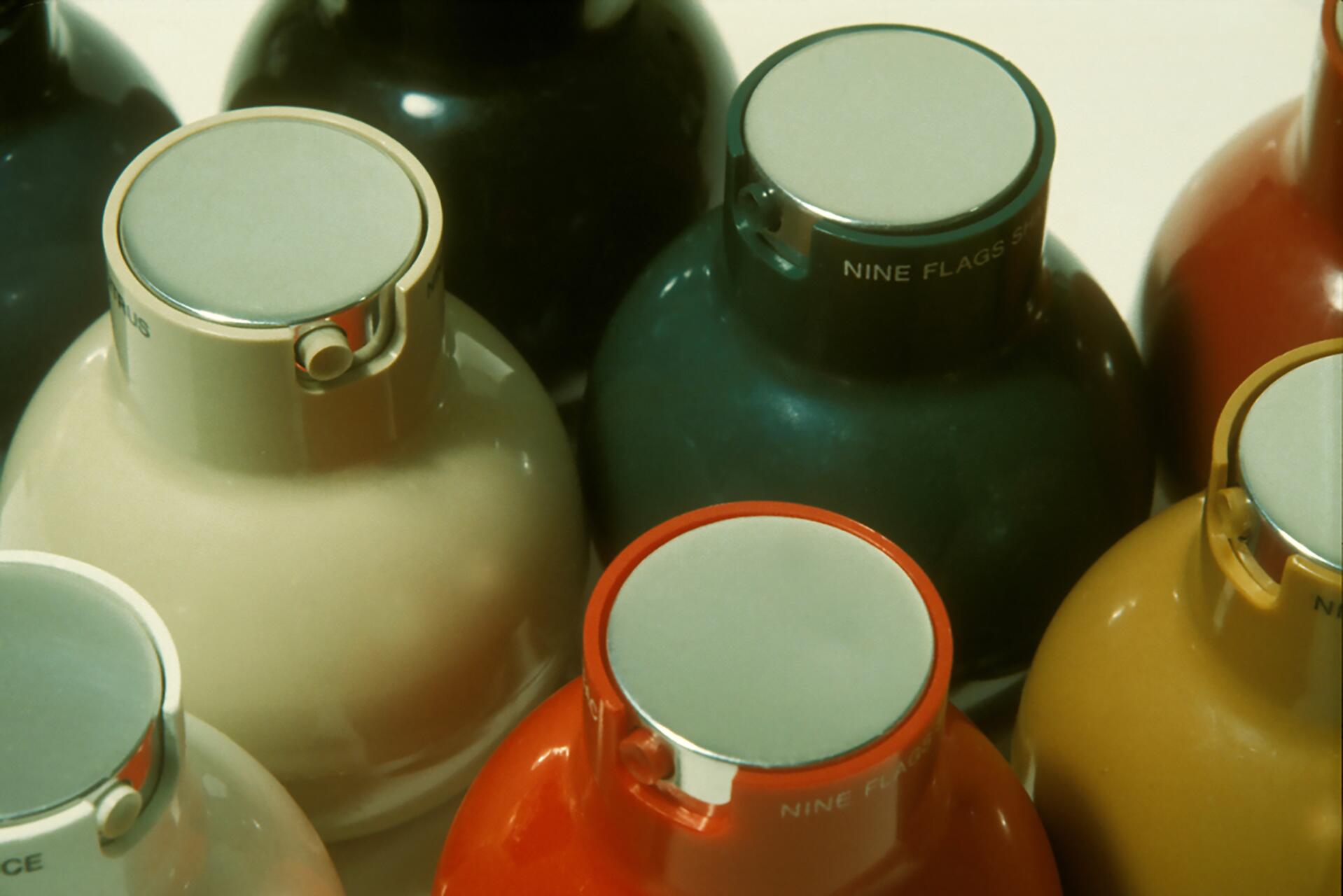 Colorful, round bottles with metal caps viewed from above, featuring hues of black, cream, green, and orange, arranged closely together.