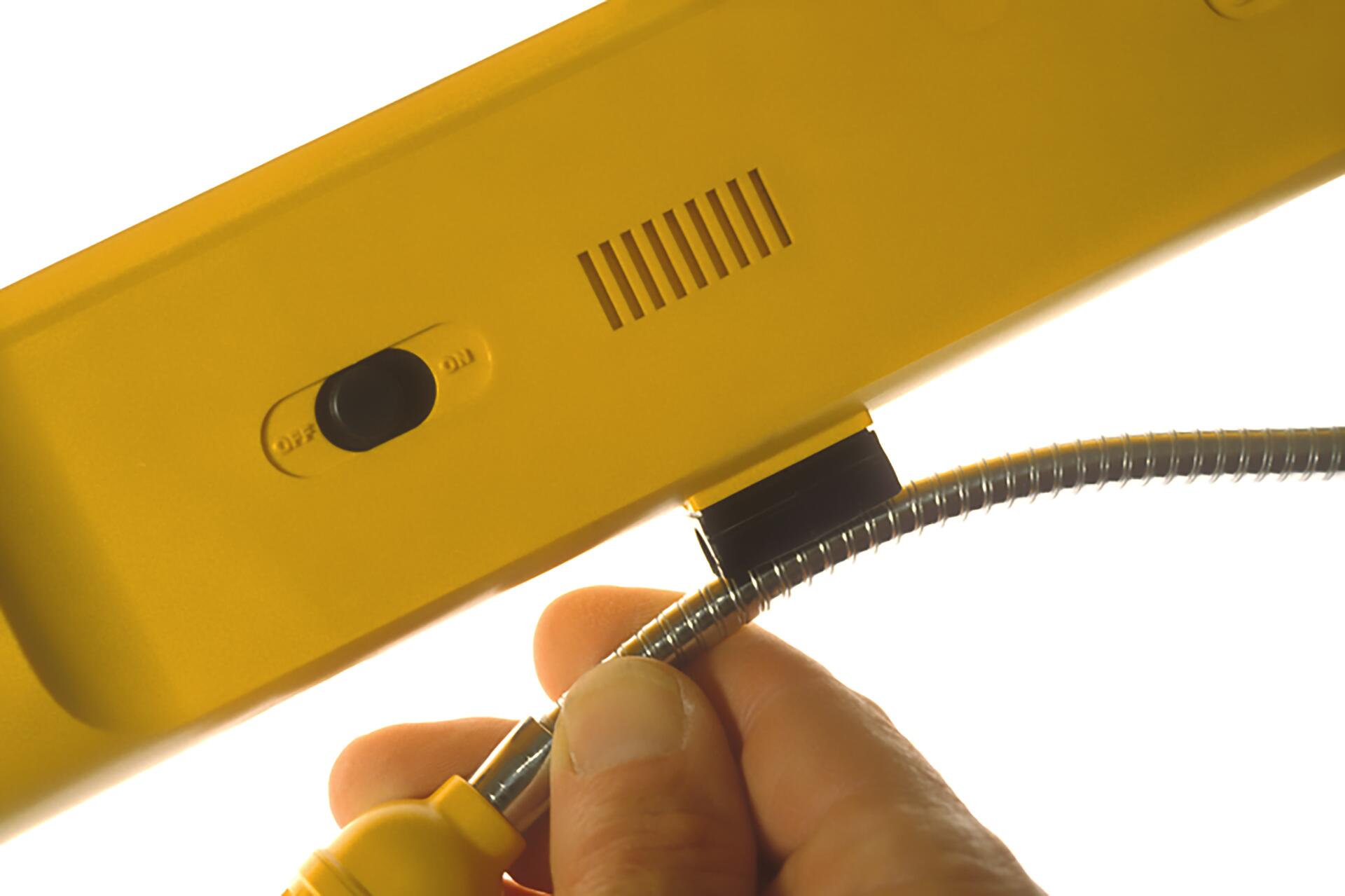 Hand holding a coiled metal hose attached to a yellow device with an on-off switch.