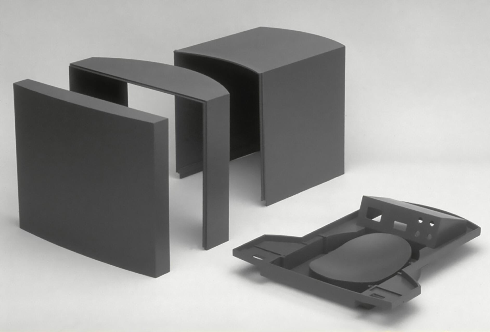 Four black geometric objects, including two curved panels and a flat piece with cutouts, arranged on a light background.