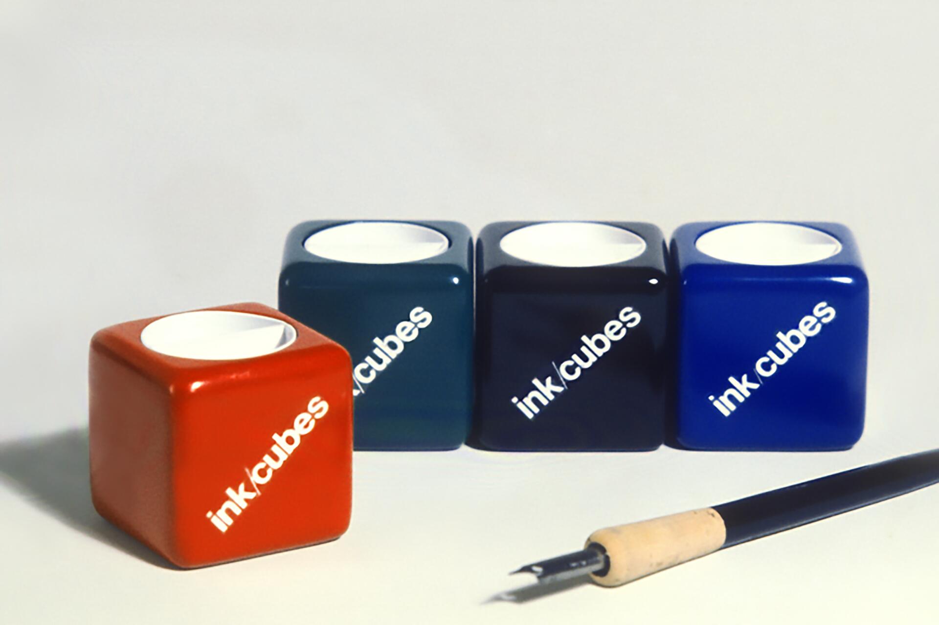 Four colorful ink cubes labeled "ink cubes" in red, teal, black, and blue, arranged in a row. A pen with a nib is in the foreground.