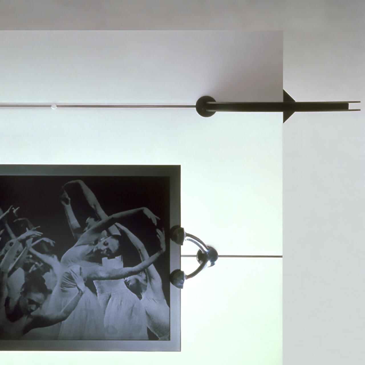 Black and white photograph of dancers in fluid motion, set against a stark white surface with geometric elements and a large black arrow pointing right.
