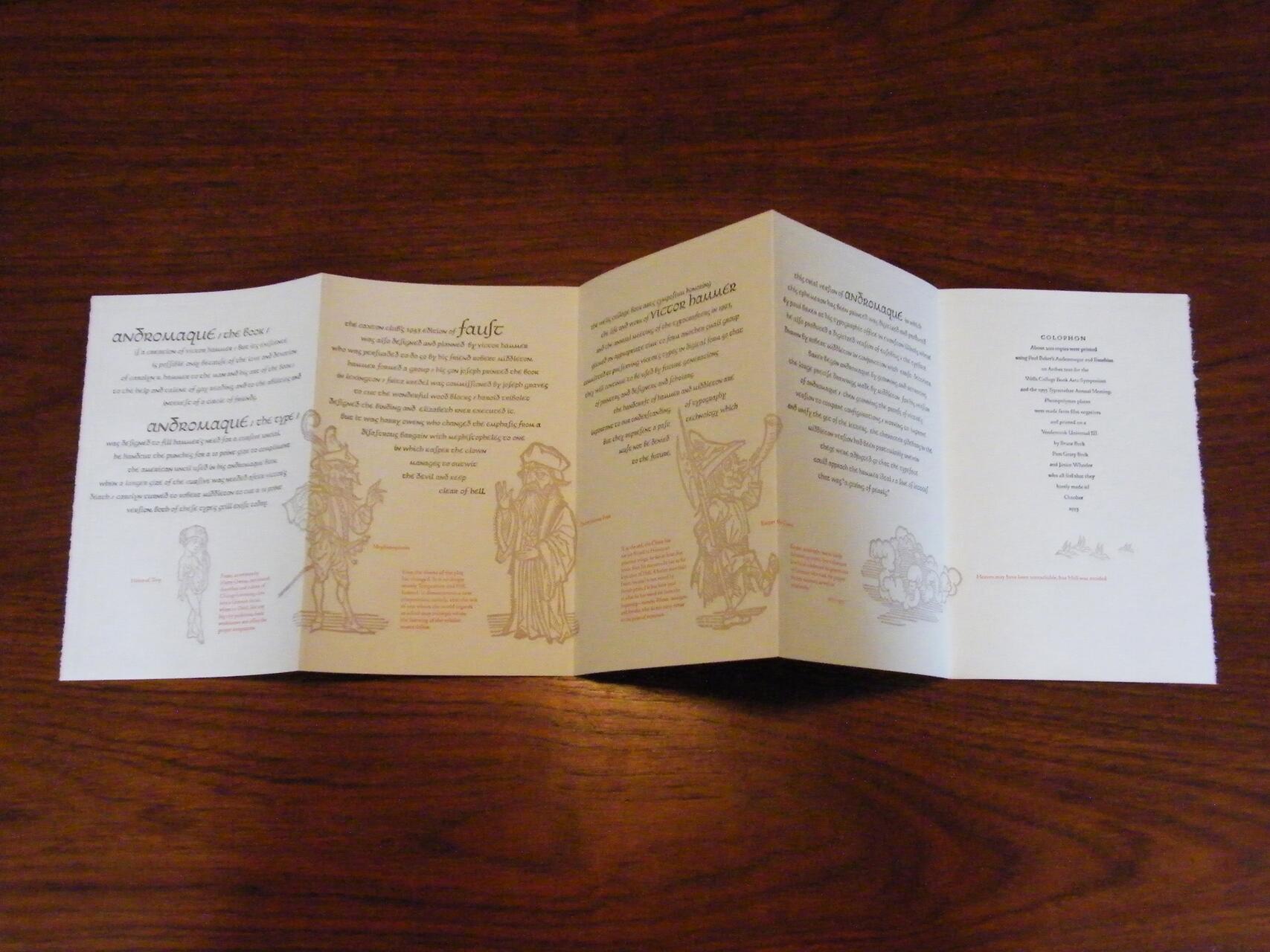 Folded brochure with text and illustrations on a wooden table. The brochure features artistic drawings of historical figures and decorative elements with text in multiple columns.