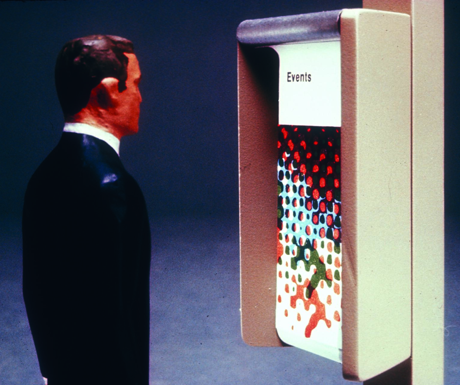 A sculpture of a man in a suit looks at a wall-mounted display with the word "Events" and colorful dots on the screen.