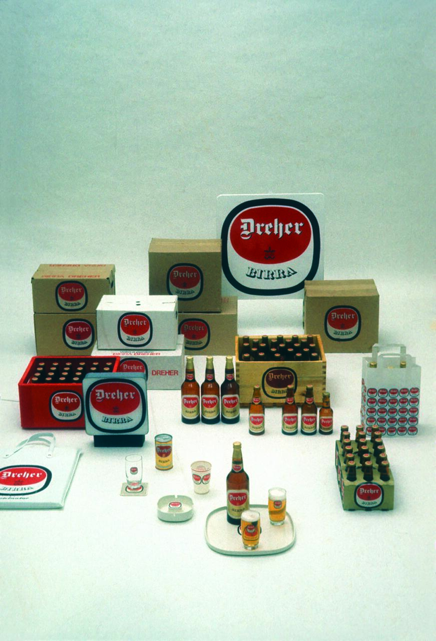 Various sizes of Dreher beer bottles and packaging arranged neatly against a plain background, including bottle crates, cans, and branded glasses, emphasizing the designs and branding.