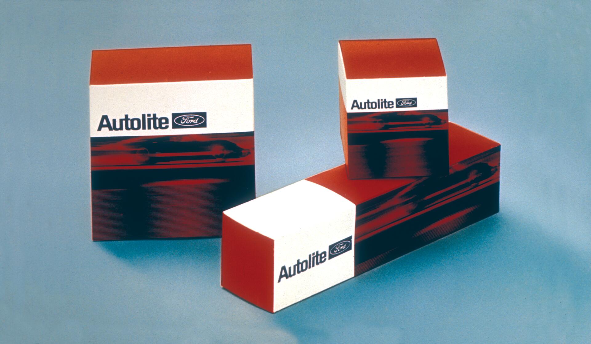 Three Autolite Ford spark plug boxes in bright red, white, and black on a light blue background.