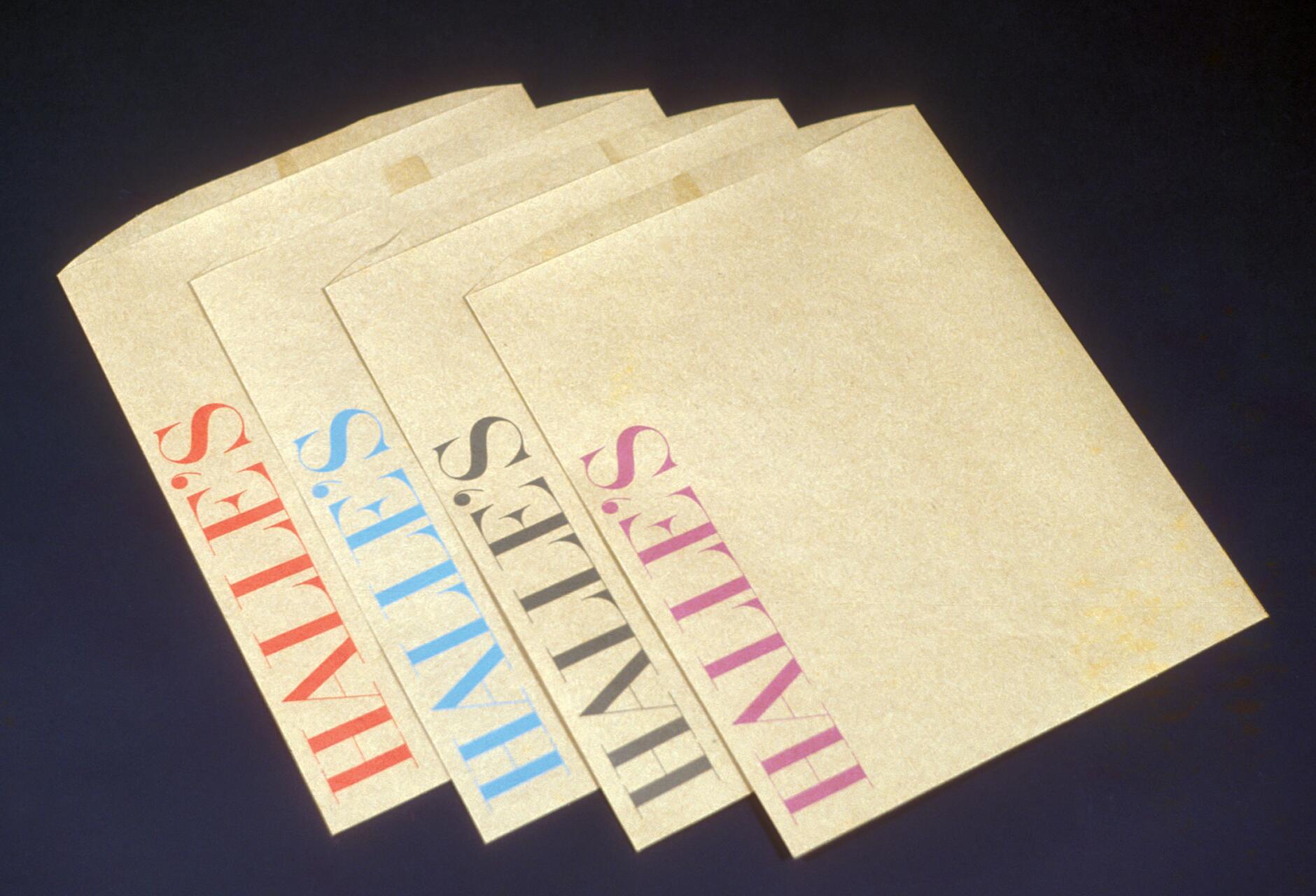 Four beige paper bags each printed with "HALLE'S" in different colors: red, blue, black, and pink, arranged slightly overlapping on a dark background.