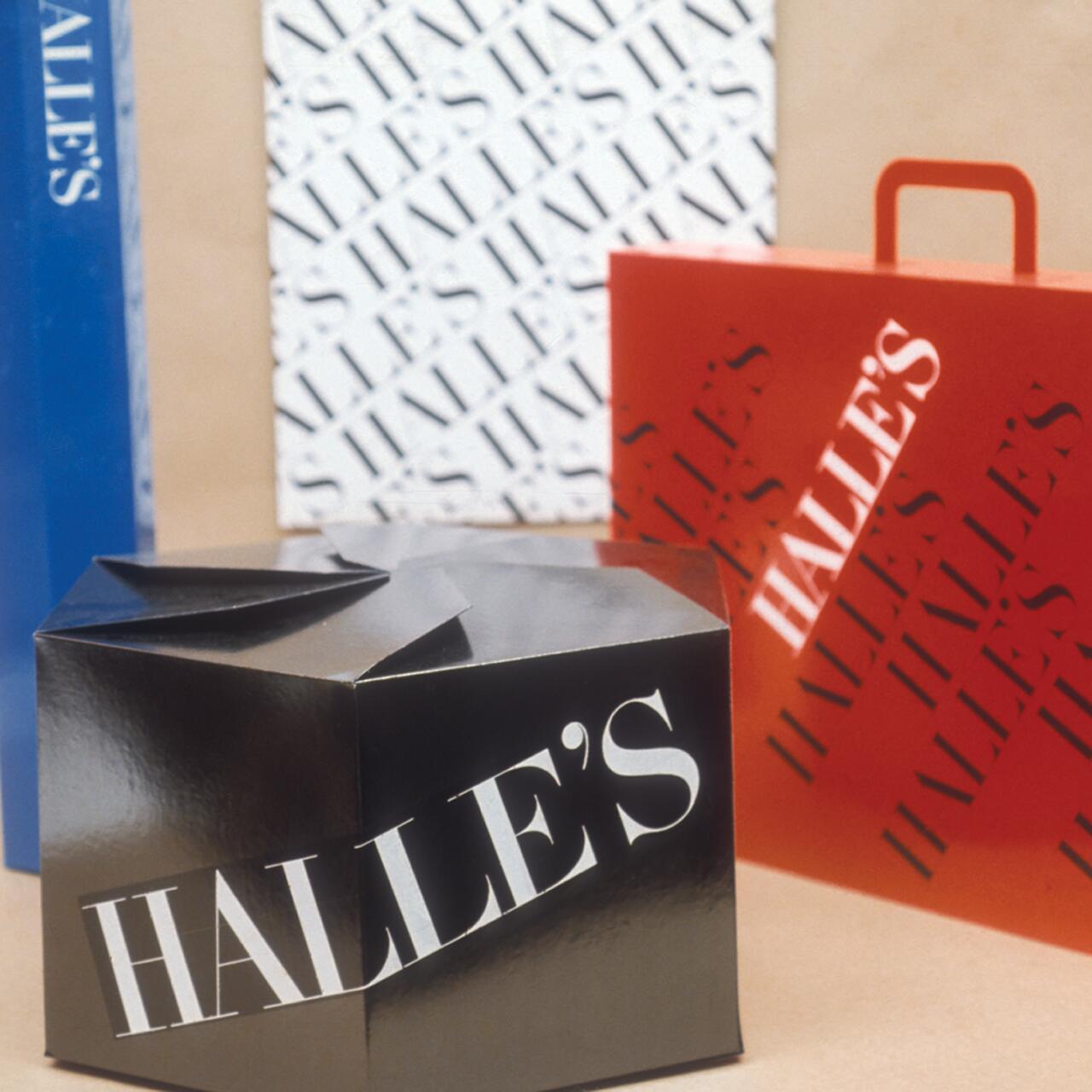 Black gift box, red shopping bag, and blue paper with the name "Halle's" in bold white text. Box has a folded top, bag has handles, and paper features a repeating pattern.