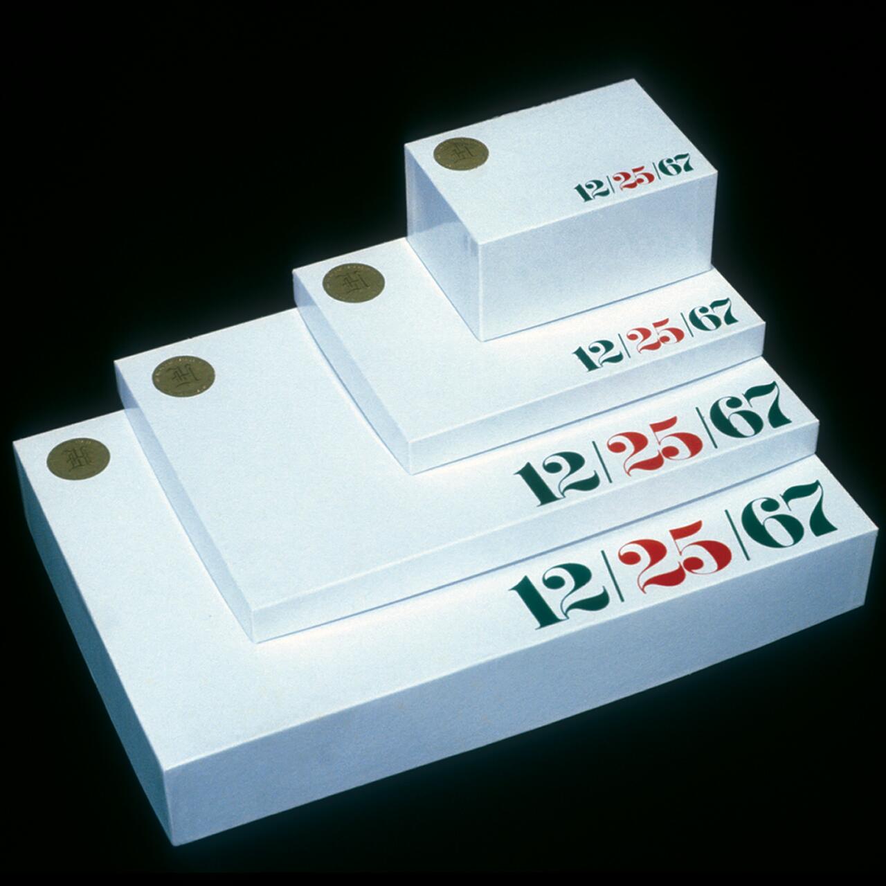 White boxes of varying sizes, stacked in a stepped arrangement against a black background. Each box has the numbers "12/25/67" in green and red on the side and a gold seal on the top corner.
