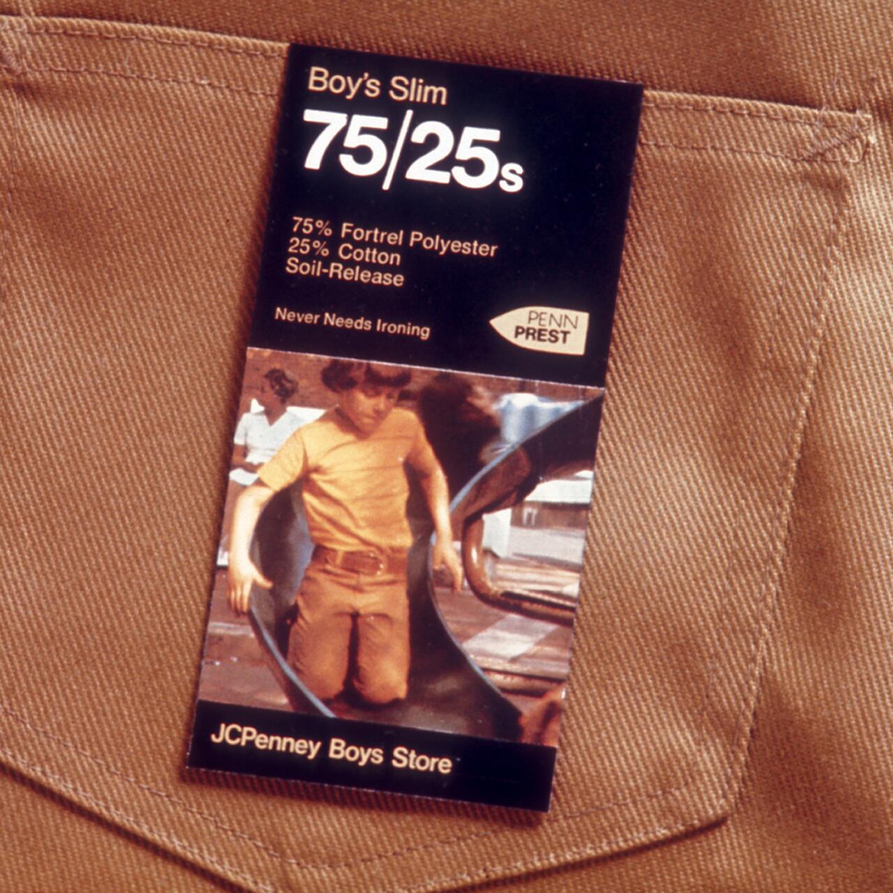 Label on brown fabric showing text about polyester and cotton blend pants from JCPenney Boys Store, with an image of a boy on a slide.