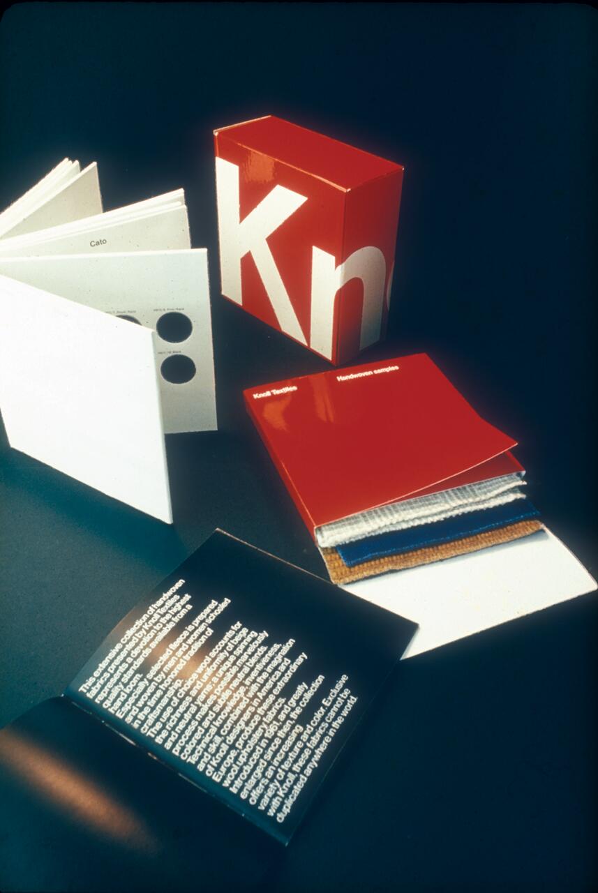 Red and white design packaging, open booklet with text, and fabric swatches on a dark background.