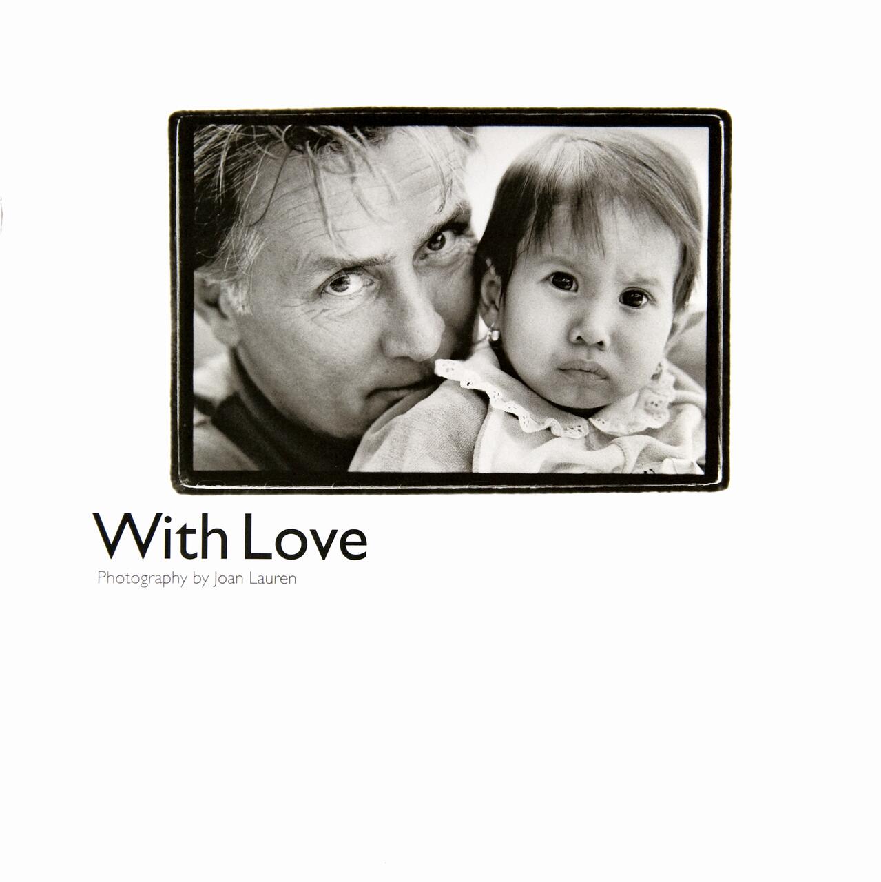 Black and white photograph of an adult closely hugging a baby, both looking at the camera with gentle expressions. Text below reads "With Love. Photography by Joan Lauren."