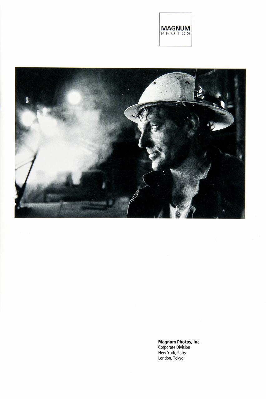 Black and white photograph of a man in a hard hat, side profile, with a focused expression. Industrial setting with smoke in the background. Magnum Photos logo at the top.