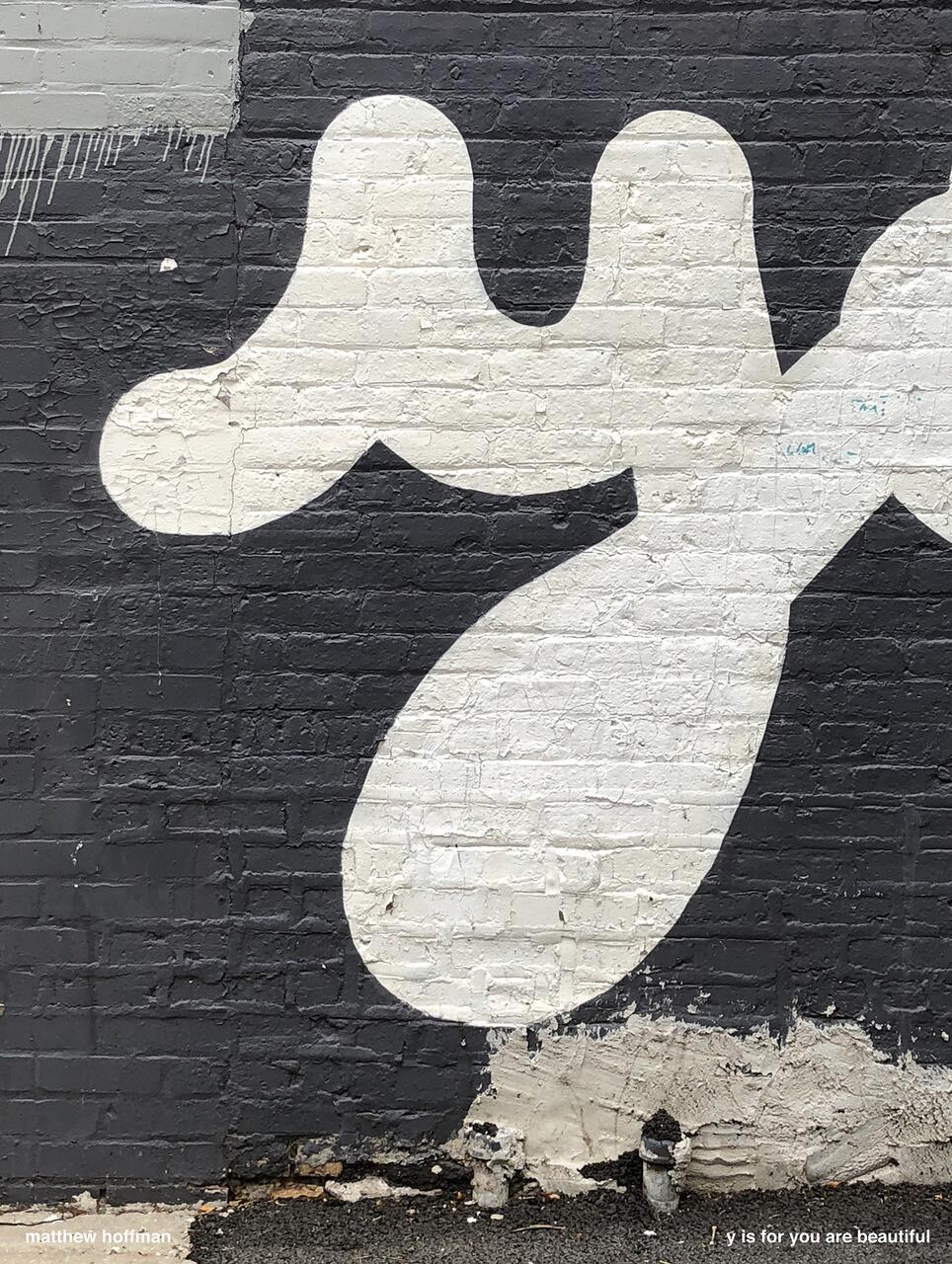 White abstract shapes painted on a dark gray brick wall with rough texture.