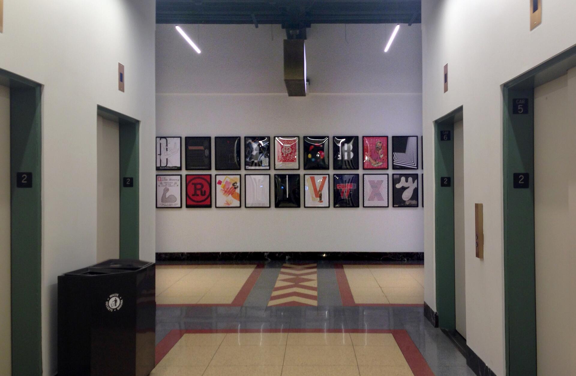 Corridor with elevators on either side, walls decorated with framed colorful artwork.