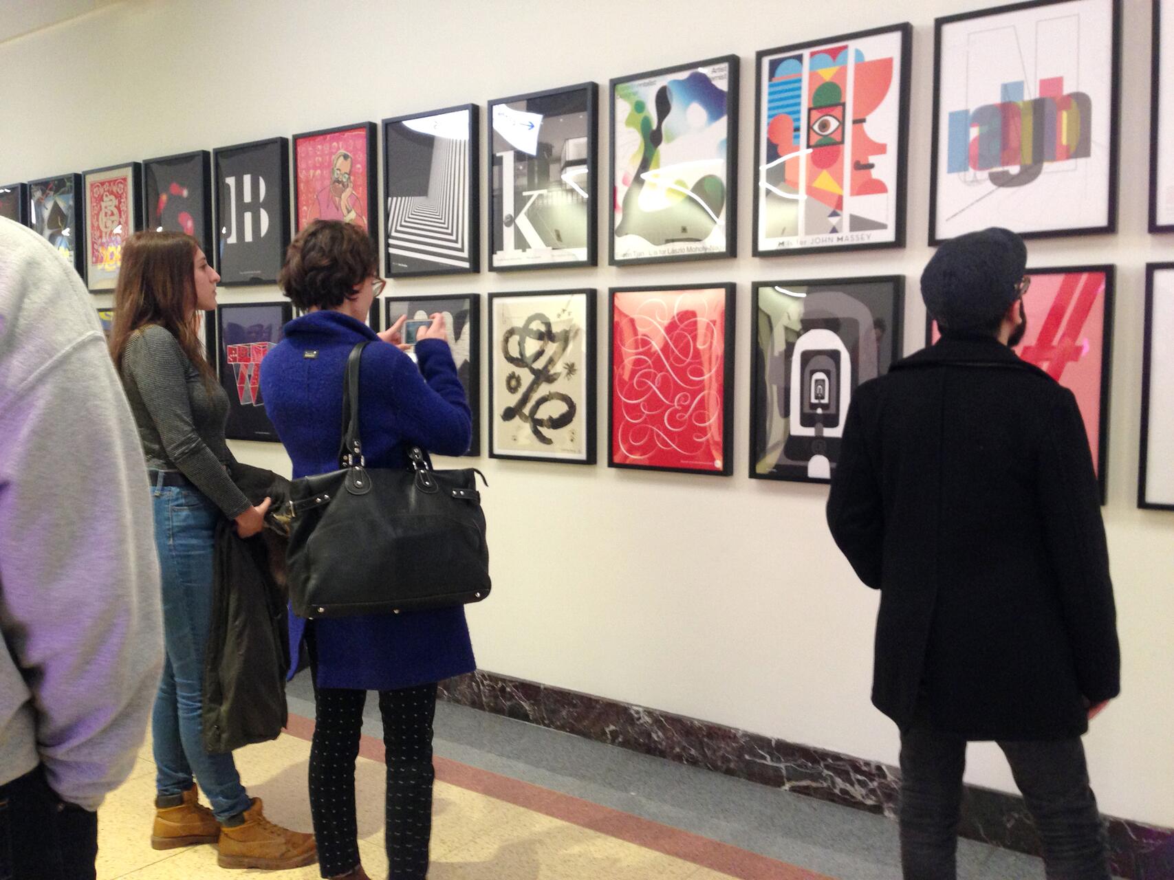 Three people view colorful art prints on a gallery wall.