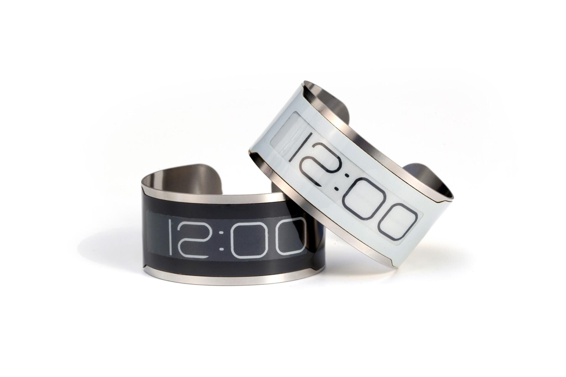 Two digital wristbands with metallic edges, displaying "12:00" on a white and black background.