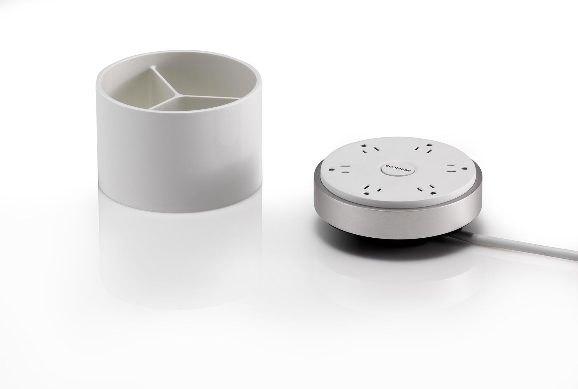 White cylindrical container with three compartments on the left, next to a round, metallic power hub with multiple sockets and a cord on the right, set against a white background.